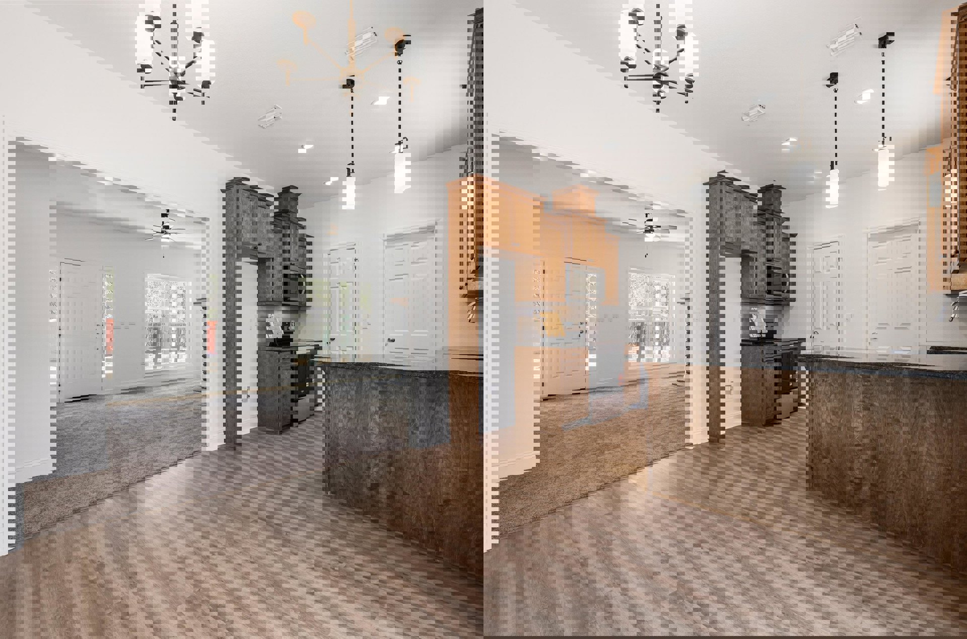 Open-concept kitchen and living room featuring hardwood floors, white cabinetry, built-in microwave, stone countertops, modern chandelier, white door with silver handle, and a