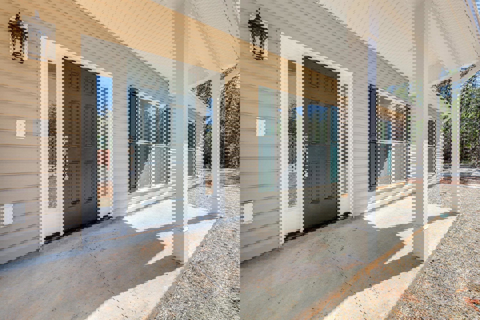 Covered front porch with white siding, dark wood door featuring a modern lock, adjacent window, wall-mounted light fixture, and white light switch panel
