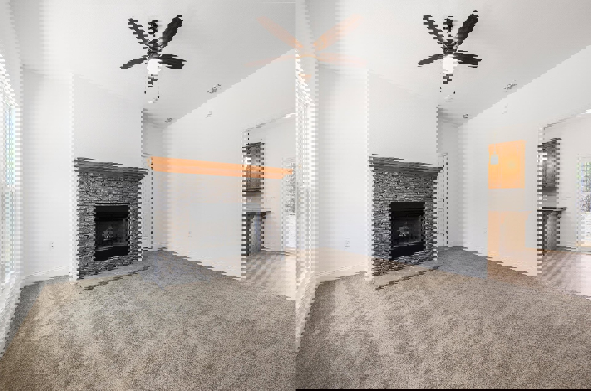 Living room with beige carpet, wood-framed fireplace, ceiling fan with light, black shelf holding a white roll of paper