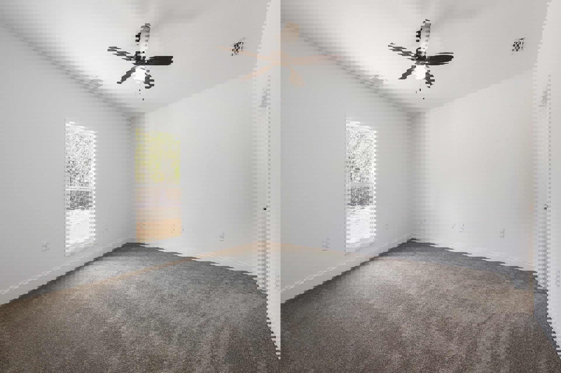 Carpeted room with white walls, ceiling fan with light, window showing trees and dirt field outside, wall vent visible
