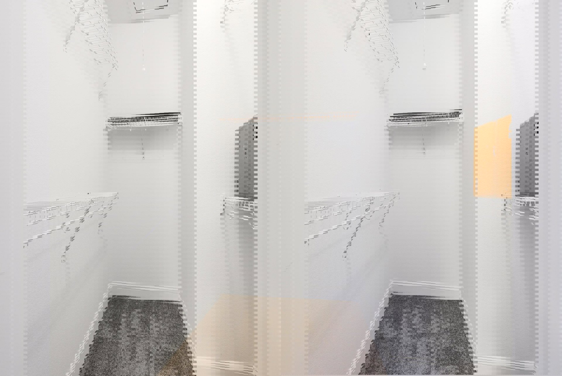 White closet with built-in shelves, white carpet flooring, and a white wire shelf with a curved handle.