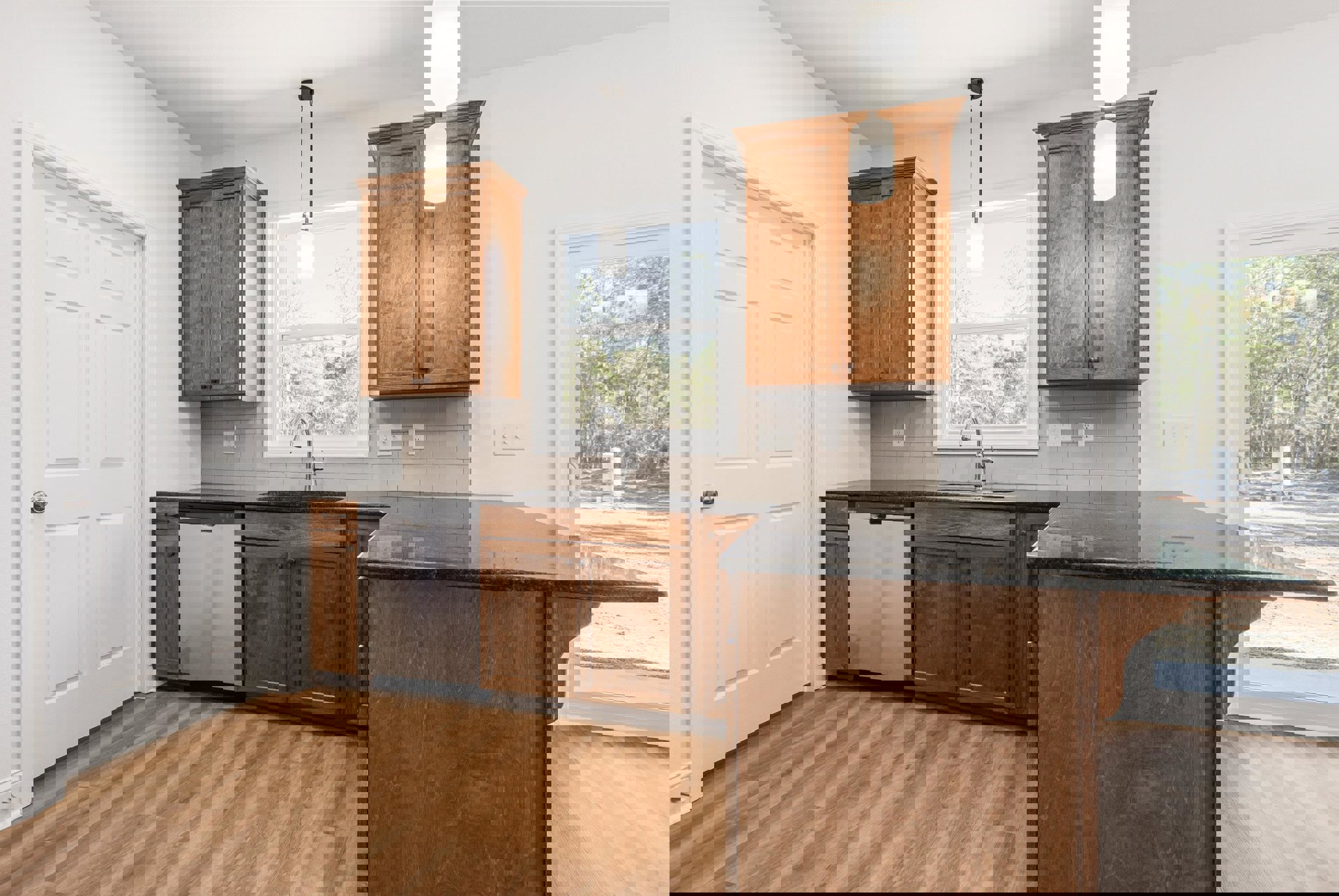 Kitchen with natural wood cabinets, stainless steel sink, white walls, ceiling light fixture, window, and white door with silver knob.