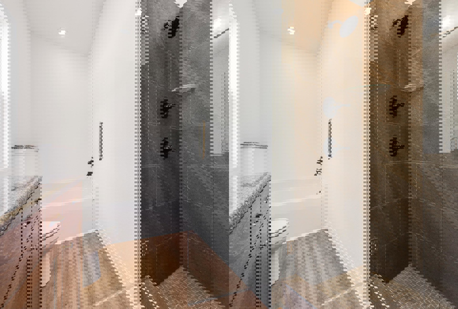 Modern bathroom featuring a frameless glass shower enclosure, white toilet, quartz countertop with undermount sink, matte black shower head, chrome faucet, and light wood