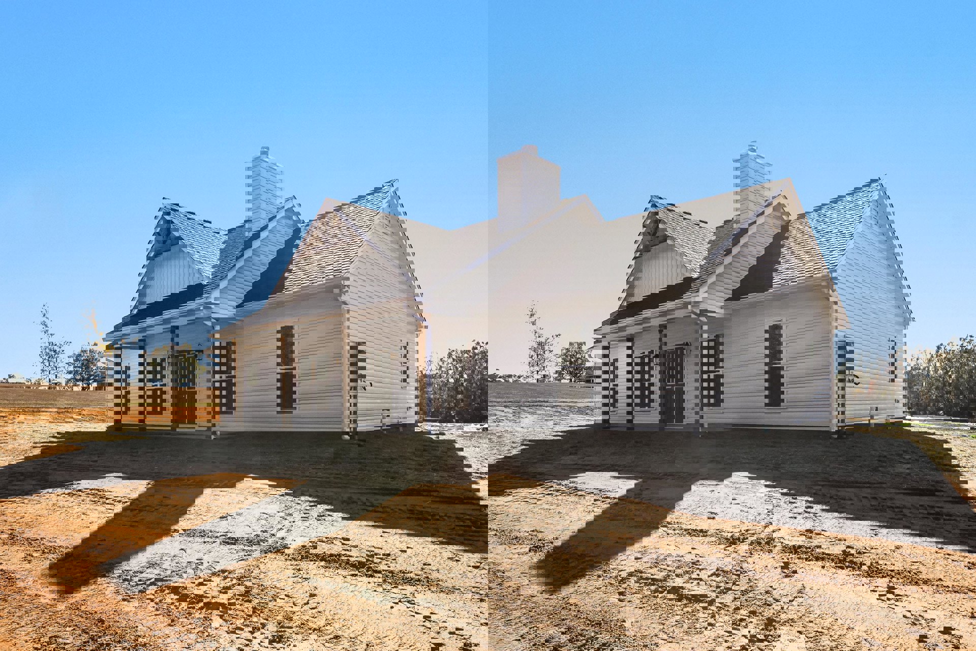 Two-story house with white-framed windows, brick chimney, and expansive grassy yard; dirt area with tire tracks in foreground; cluster of mature trees and historic Robert Frost