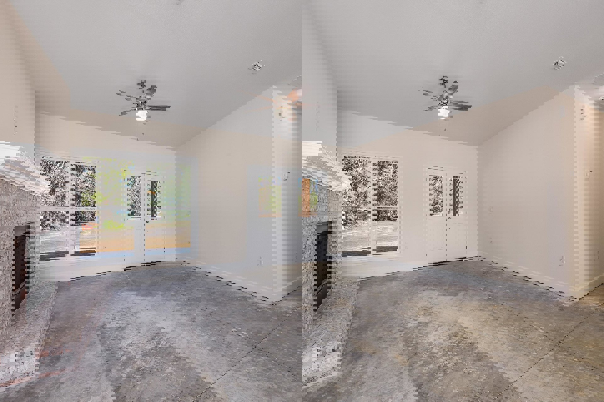 Living room with plaster walls, ceiling fan with light, double white doors, large window overlooking trees, concrete floor, and mirrored accent near entry.