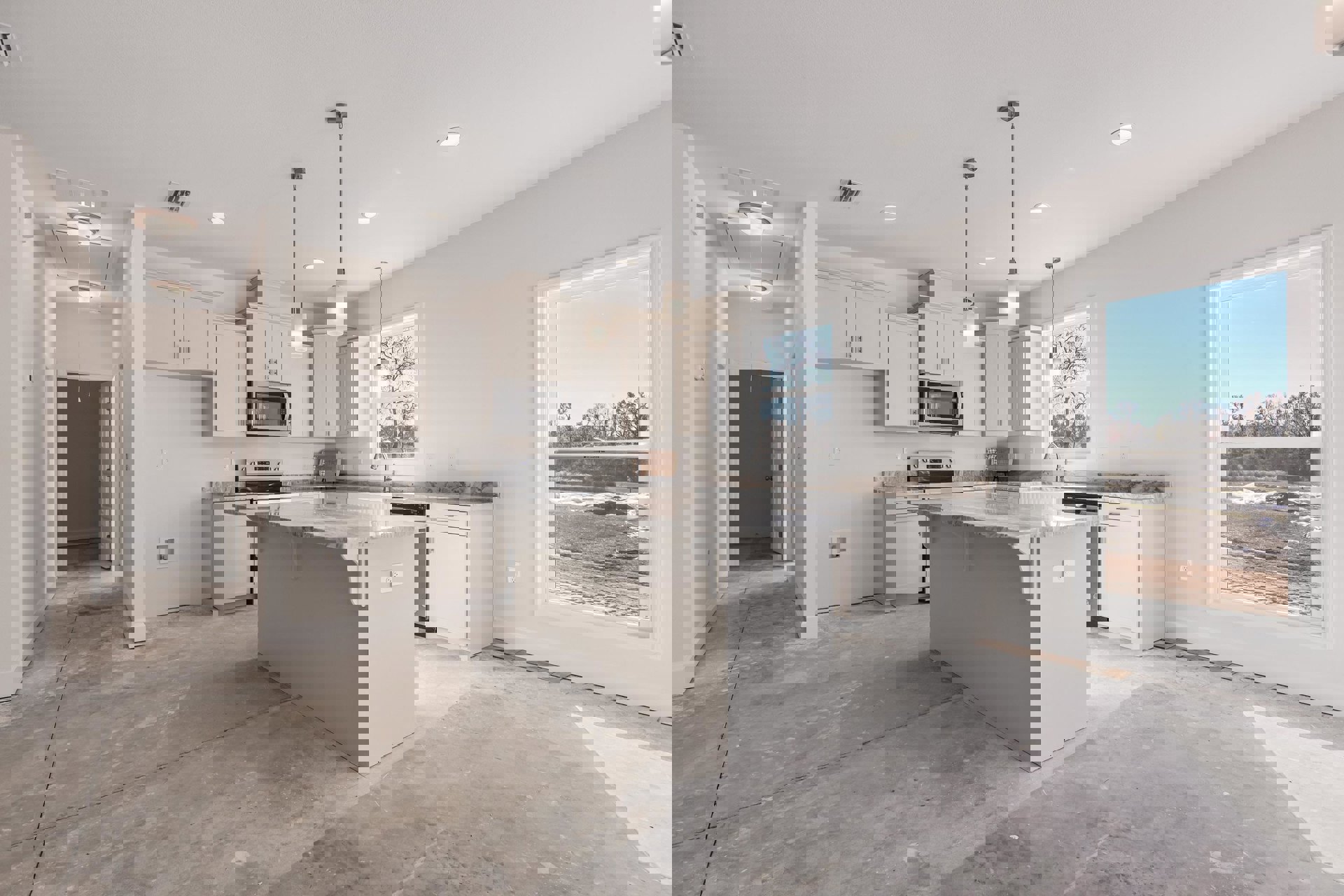 Spacious kitchen featuring a marble-topped island, white cabinetry, built-in microwave with glass door, stainless steel sink, and large window overlooking a field and trees.