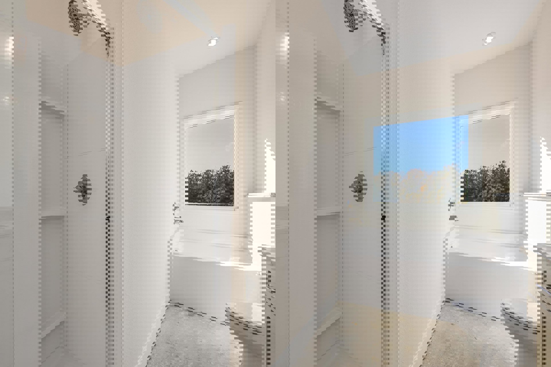 Bathroom with white bathtub and toilet, glass shower enclosure, wall-mounted sink, large window overlooking trees, chrome fixtures, light tile walls, and a round door knob on white