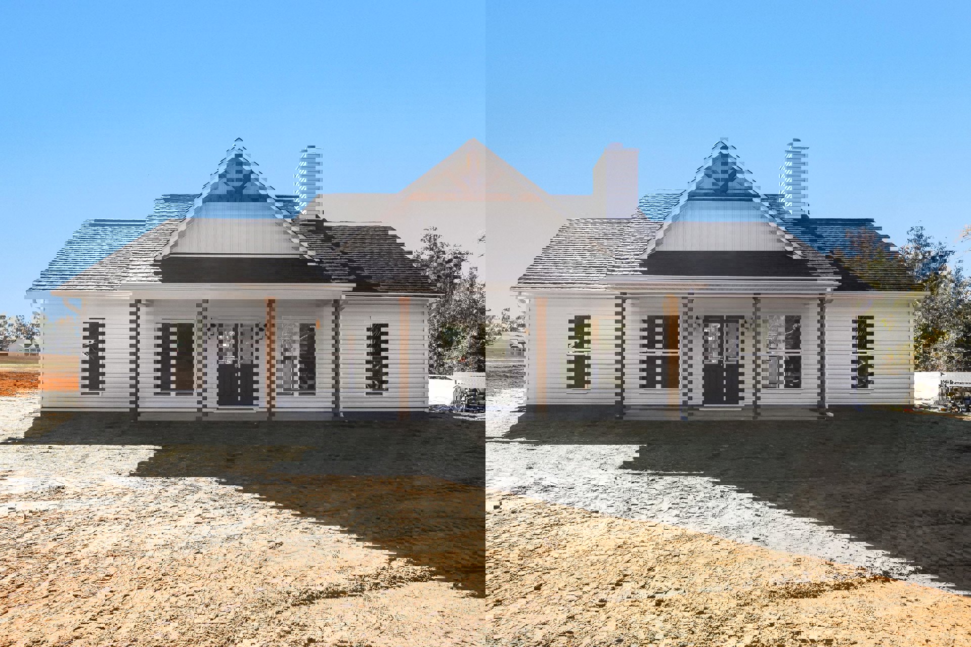 White two-story home with double front doors, white-framed windows, and a dirt yard; gray roof and small porch visible.