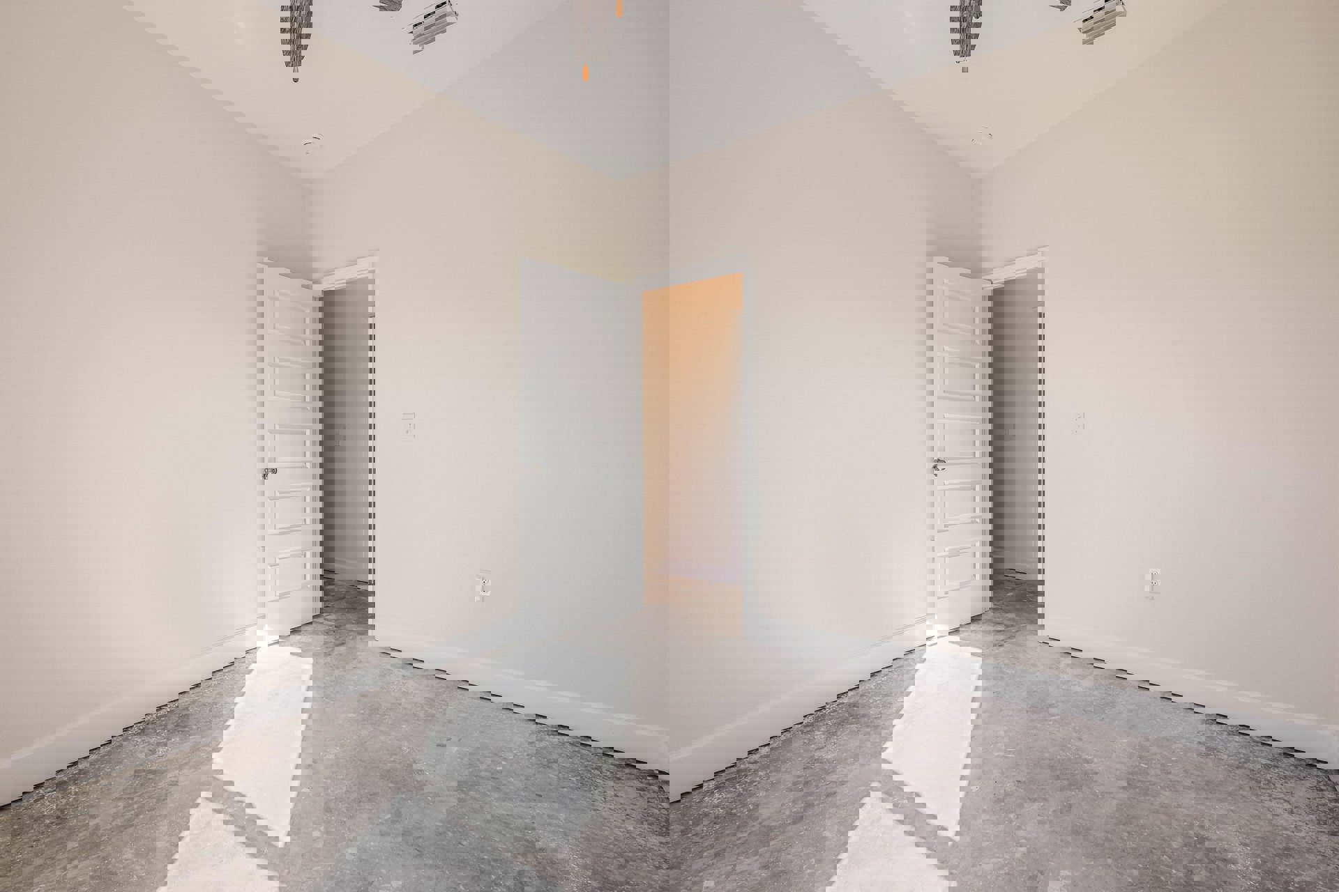 White paneled door with brushed metal handle, ceiling fan with dark blades, light gray plaster walls, white baseboard molding, concrete floor with white mat, rectangular air vent