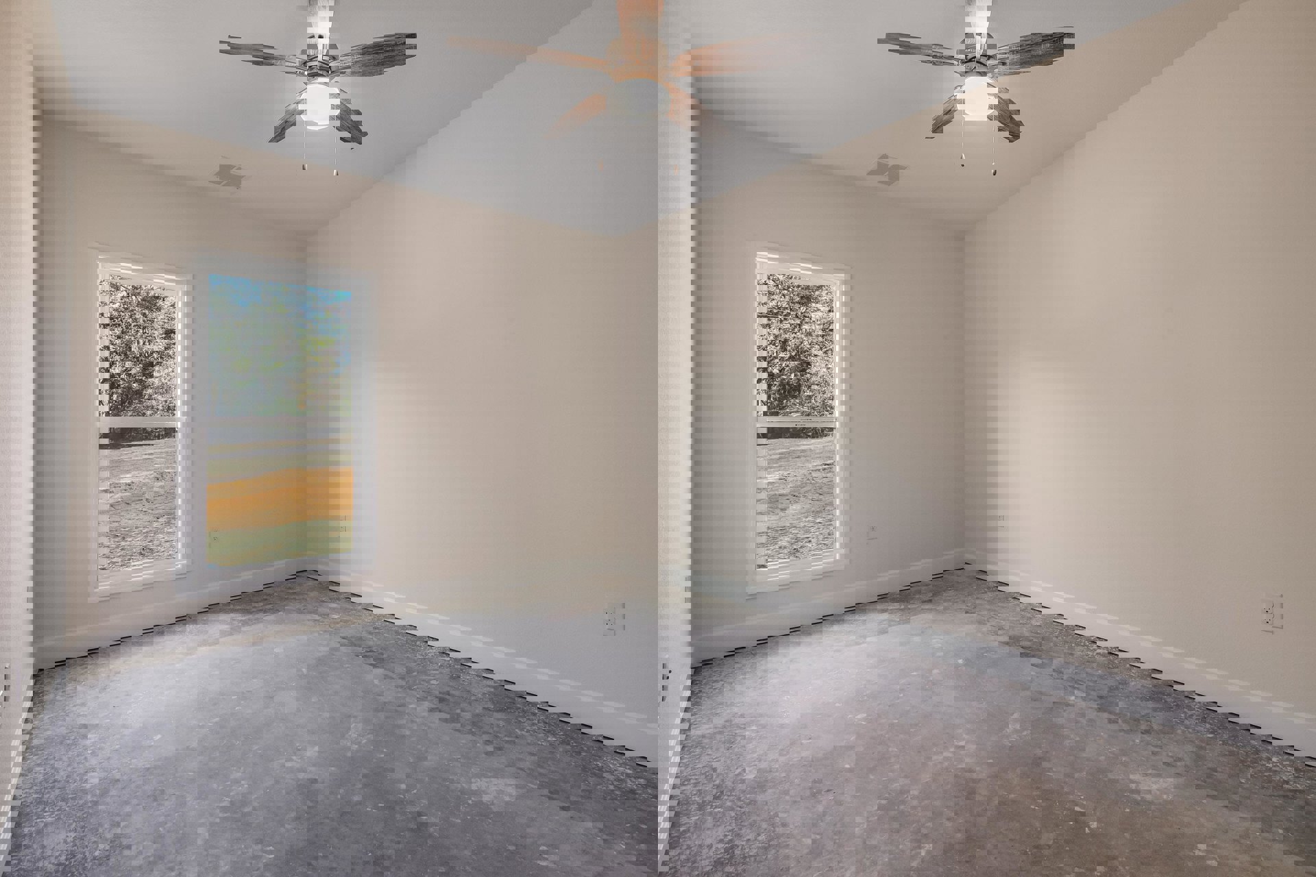 Ceiling fan with light fixture mounted above grey flooring and white walls, large window showing trees and dirt outside