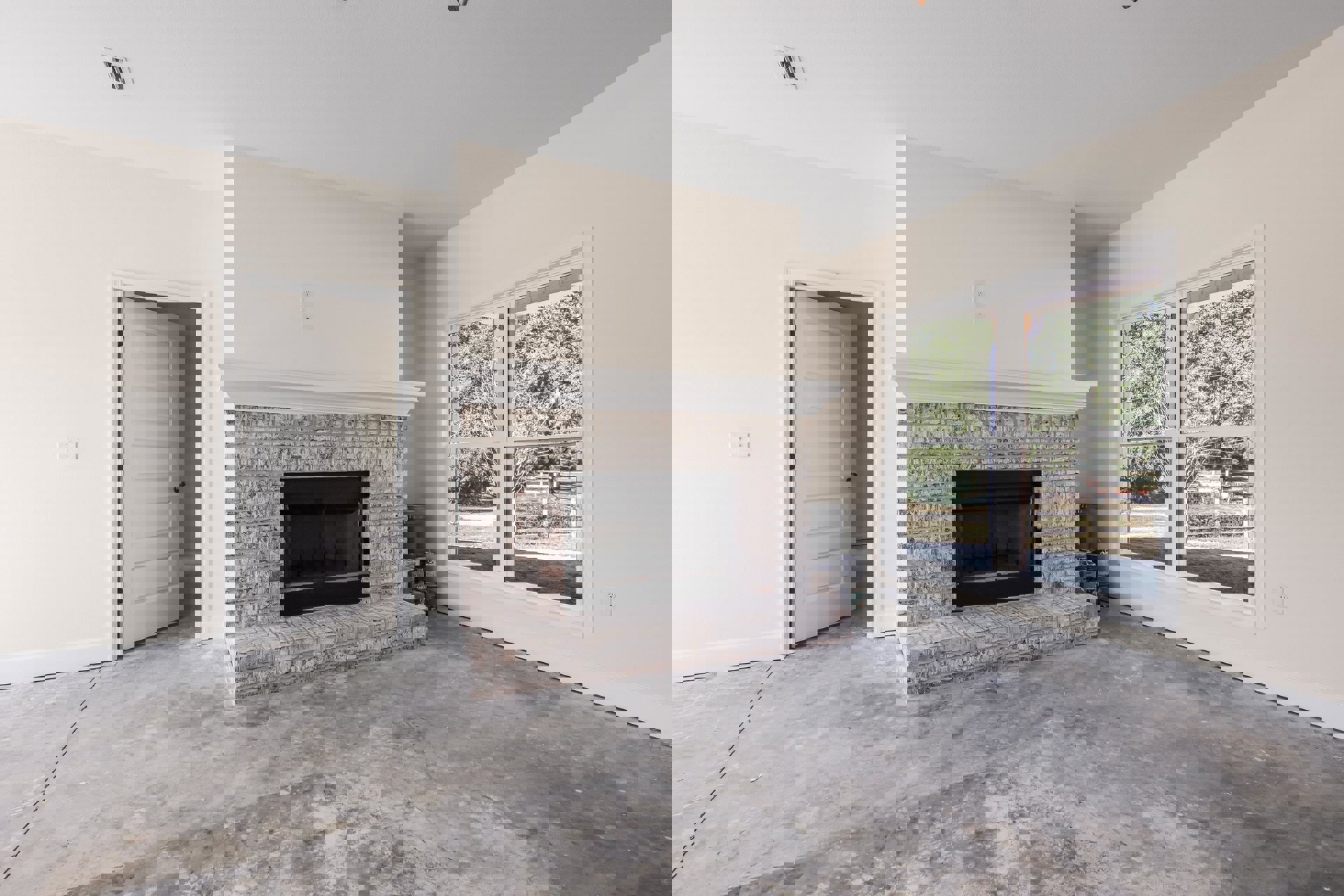 Brick fireplace with black glass door set in a plaster wall, white door with silver knob to the side, window overlooking trees, hardwood floor and white ceiling