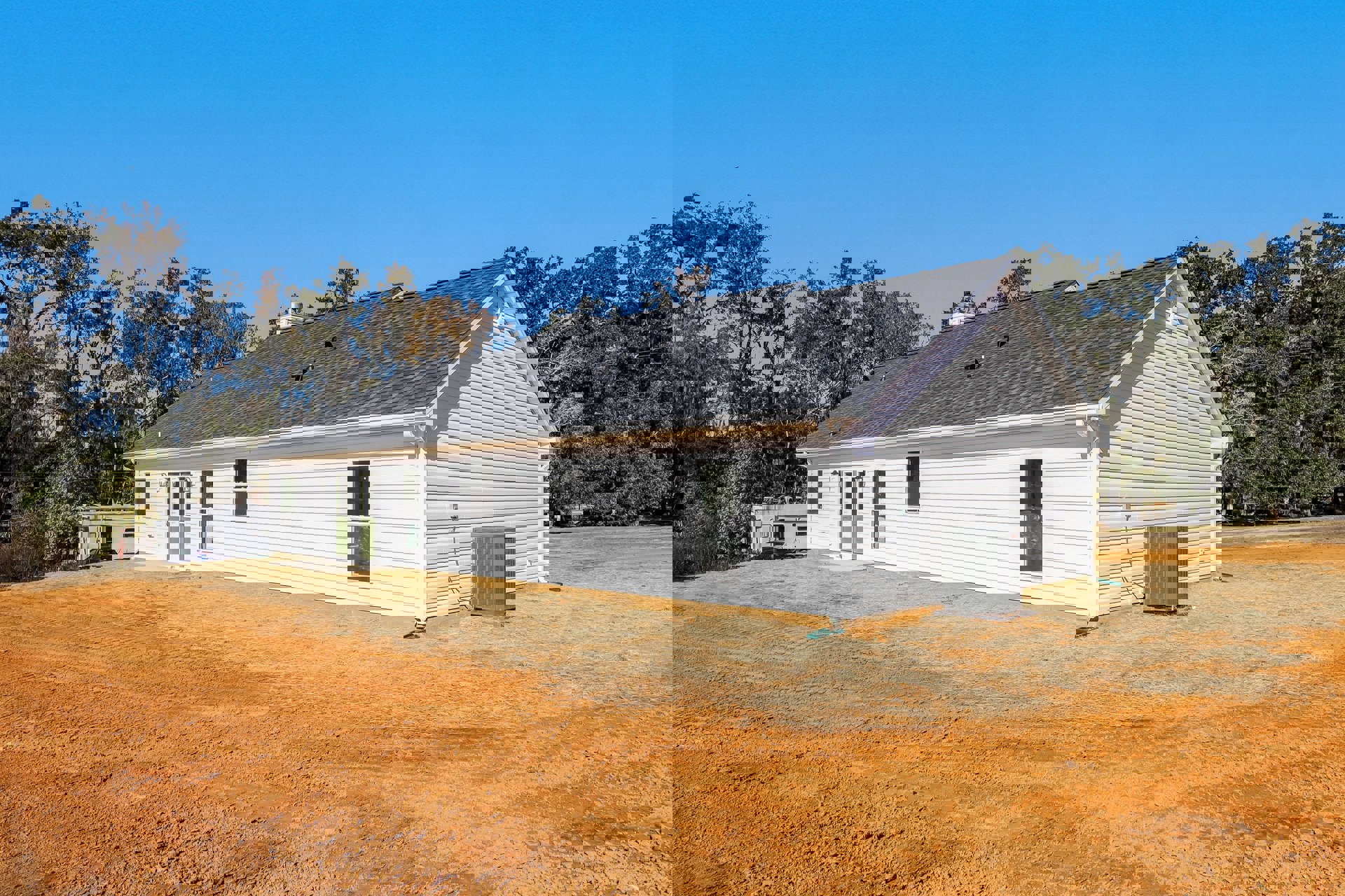 White farmhouse with black roof, white-framed windows, large grey heat pump, person standing on grass lawn, mature trees and blue sky in background
