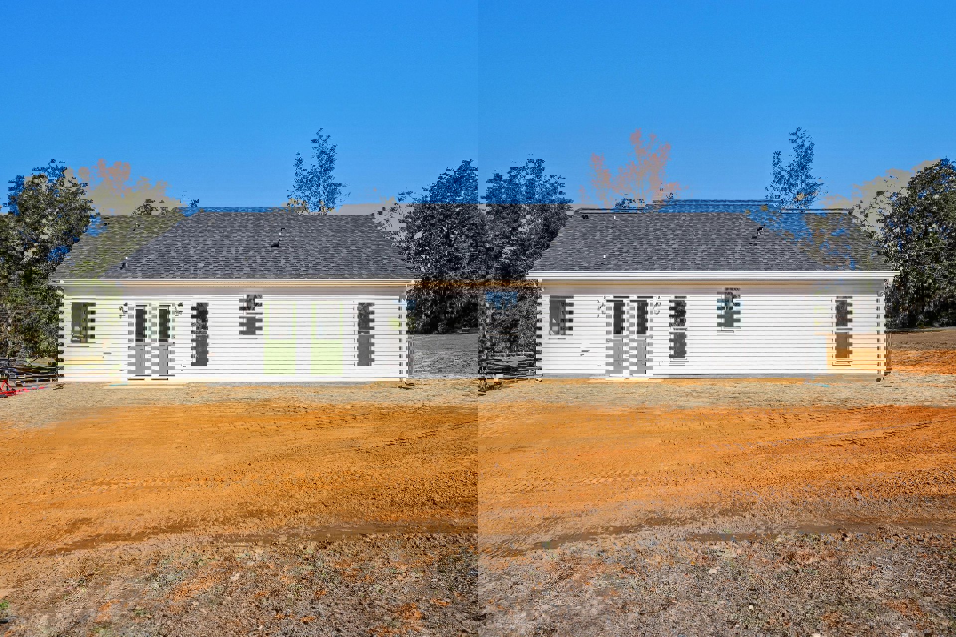 White farmhouse with green door and screened window, white-framed windows, dirt road with tire tracks, surrounded by trees and open land under blue sky