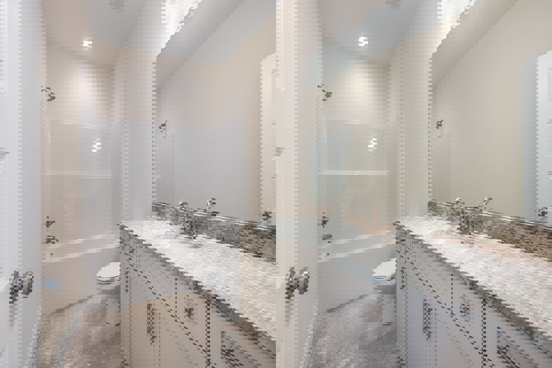 Bathroom with marble countertop sink, white toilet, glass shower enclosure, and light gray tile walls