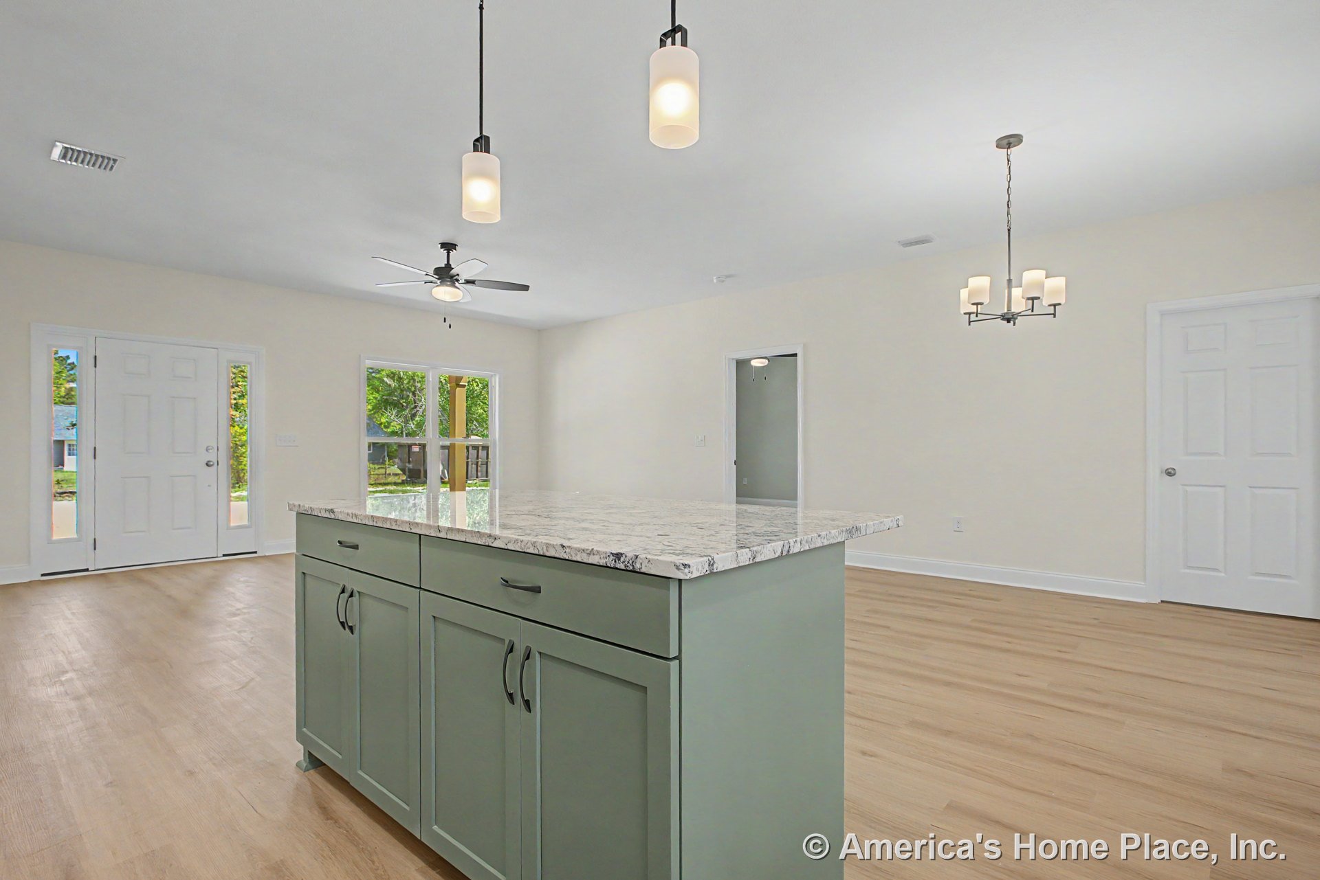 Open kitchen and living area with green shaker-style island cabinetry, marble-patterned countertop, pendant lights, light wood plank flooring, white trim and doors, large windows