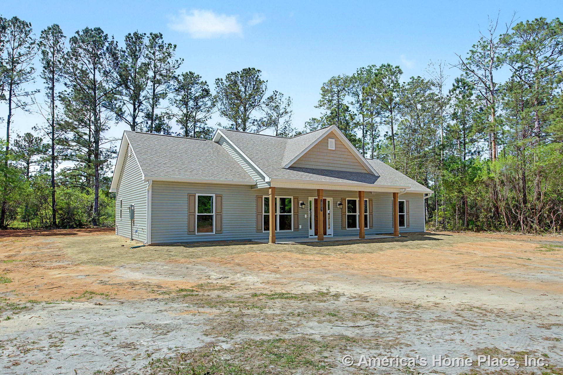 Covered front porch with wood support columns, multiple large windows, light gray vinyl siding, gable shingle roof, exterior wall-mounted lighting, and detailed trim around the