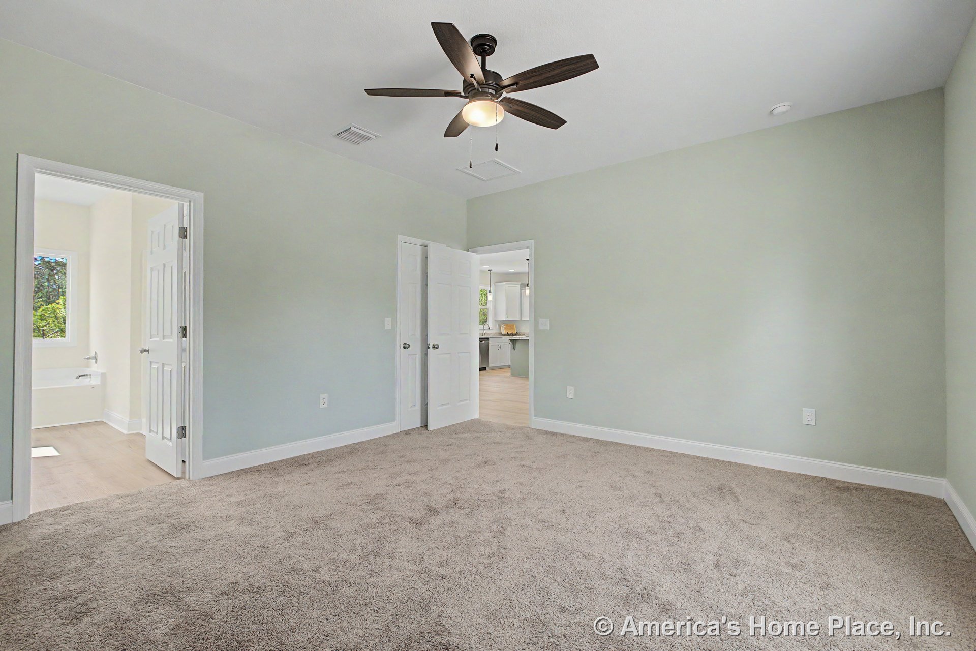 Bedroom with light carpet flooring, pale green walls, white trim and baseboards, ceiling fan with light fixture, and double doors leading to a bathroom featuring a window and