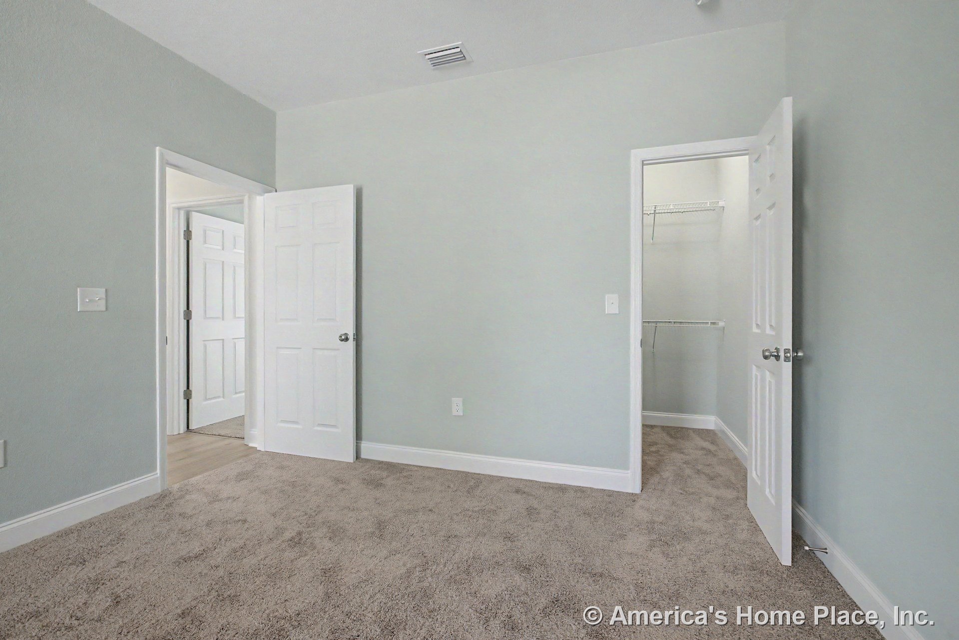 Bedroom with light gray walls, beige carpet flooring, white paneled doors, walk-in closet featuring wire shelving, white baseboards, ceiling vent, and visible door hardware and