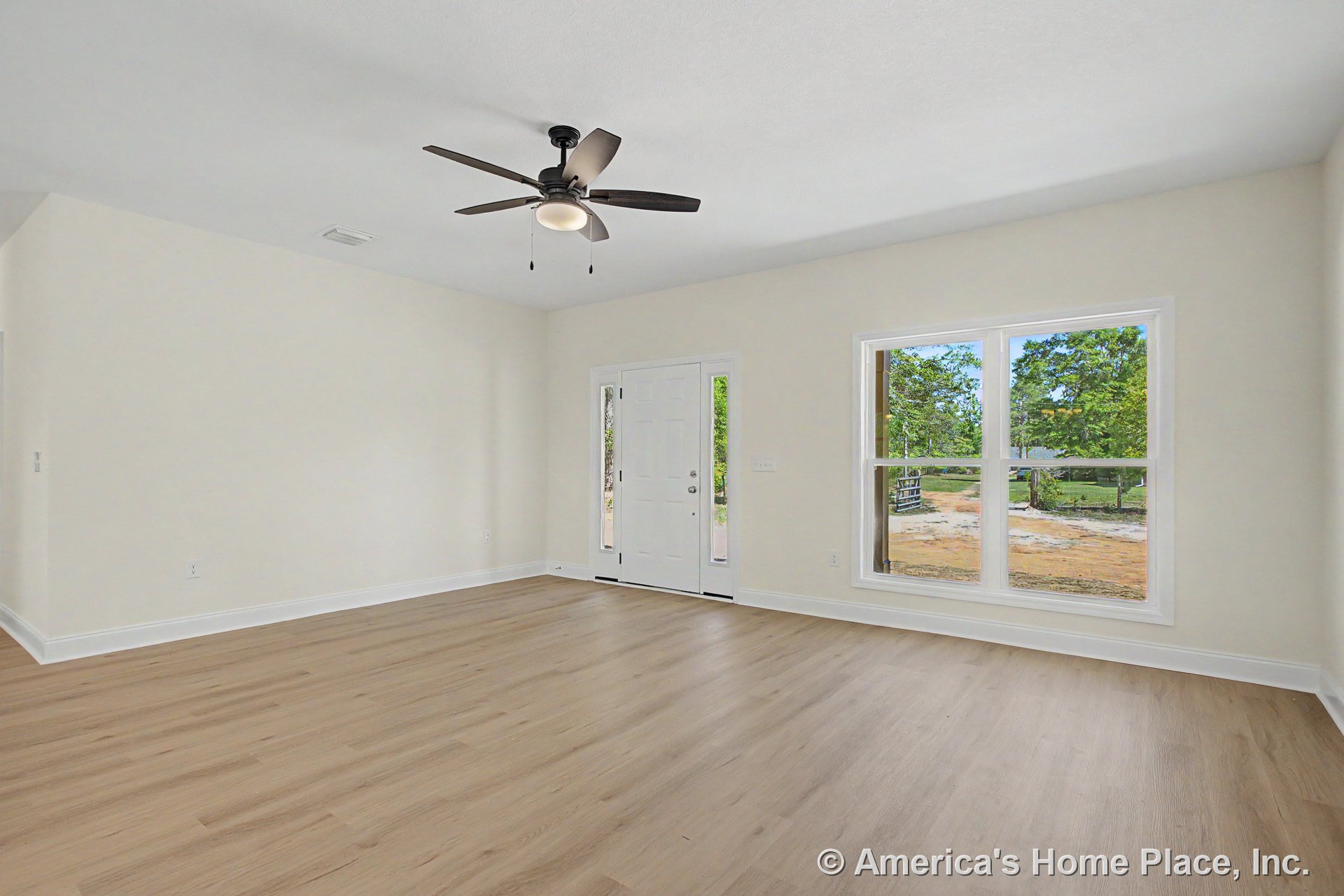 Light wood plank flooring, white trim and baseboards, large double window, white front door with sidelights, ceiling fan with built-in light fixture, and neutral wall color in a