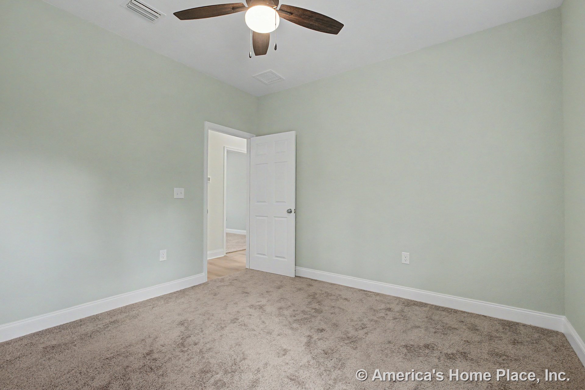 Bedroom with light green painted walls, beige carpet flooring, white baseboards, ceiling fan with integrated light, white paneled door, and ceiling vent.