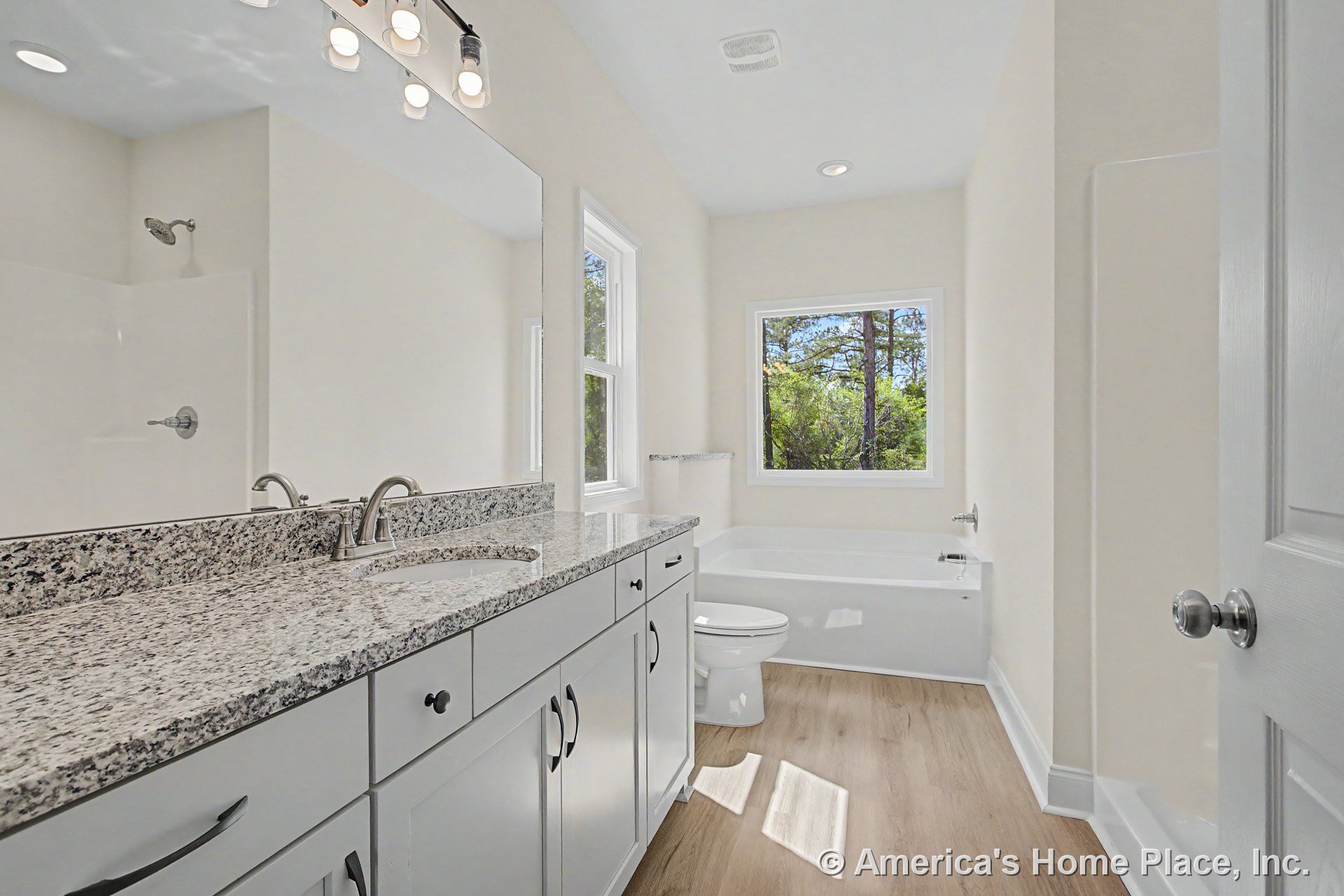 Granite countertop vanity with undermount sink and chrome fixtures, white shaker-style cabinetry, large wall mirror, soaking tub positioned beneath window, walk-in shower enclosure