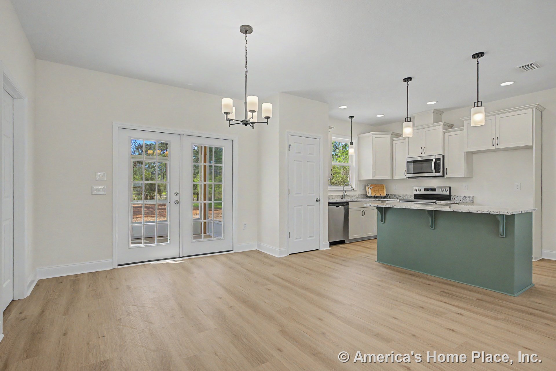 Open kitchen and dining area with light wood flooring, white upper and lower cabinets, granite countertops, green kitchen island, stainless steel appliances, pendant and chandelier