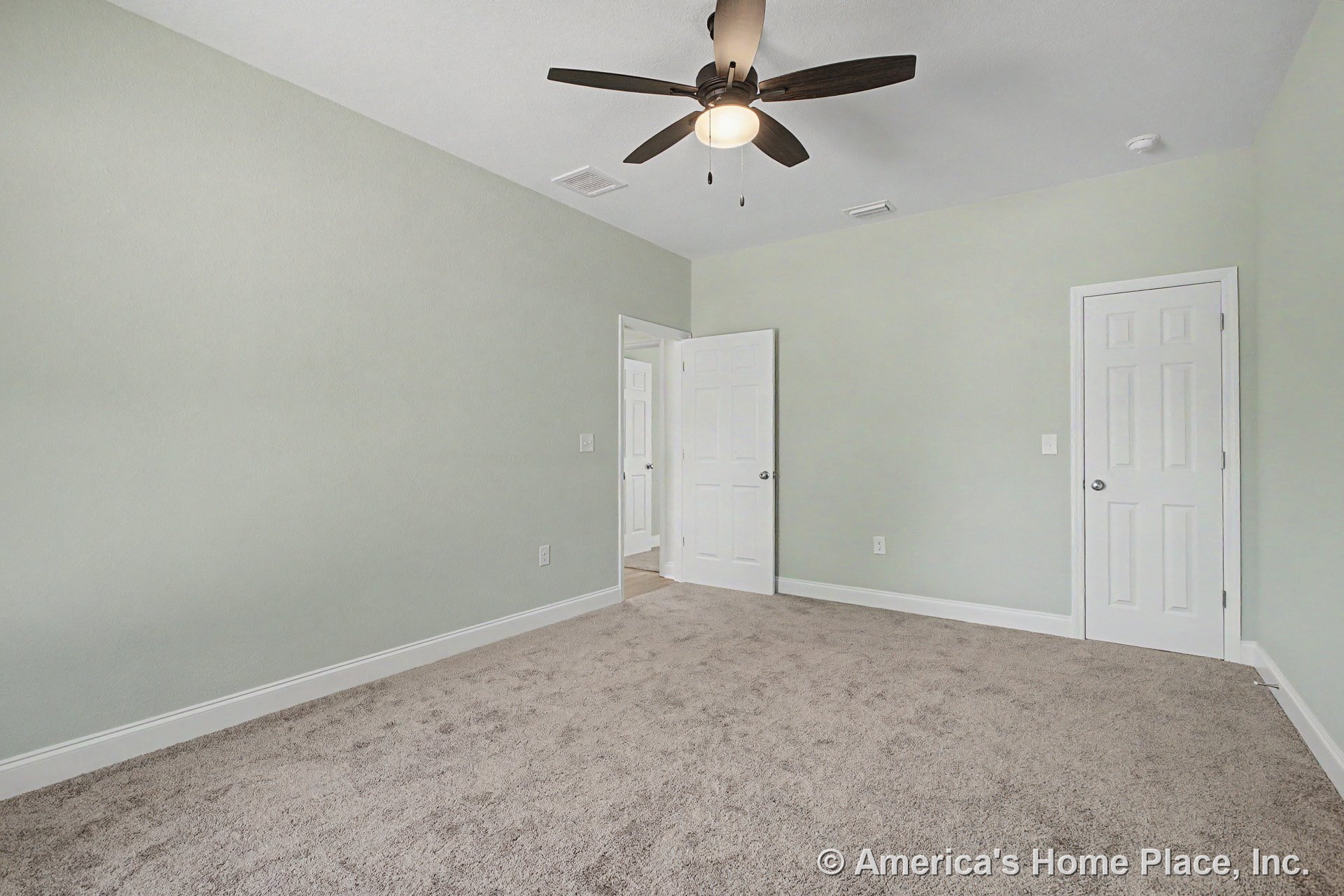 Bedroom with light carpet flooring, pale green walls, white trim and baseboards, ceiling fan with integrated light fixture, two paneled doors including a closet door, and standard