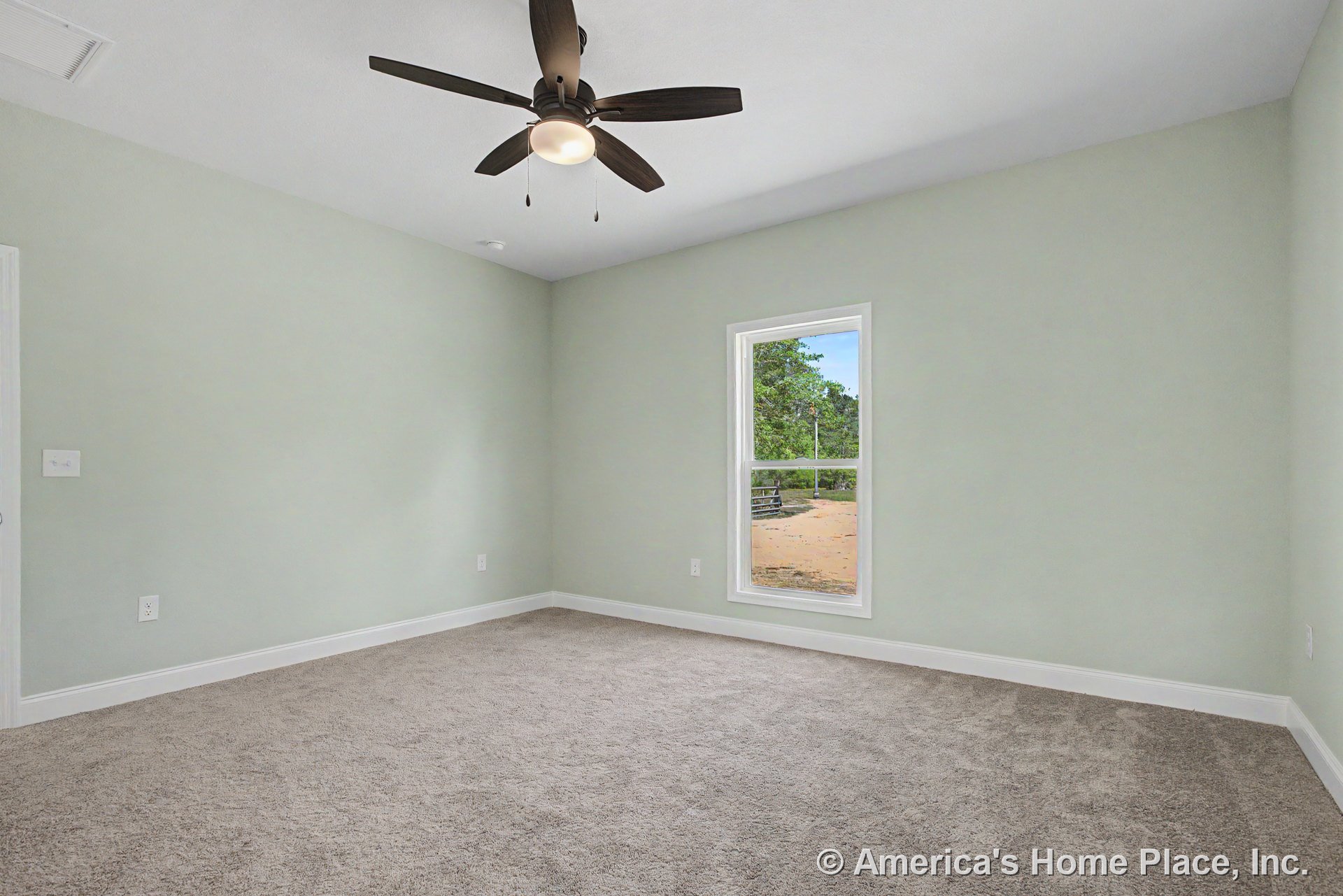 Bedroom with light green painted walls, beige carpet flooring, white trim and baseboards, single rectangular window allowing natural light, flat white ceiling, and dark ceiling fan