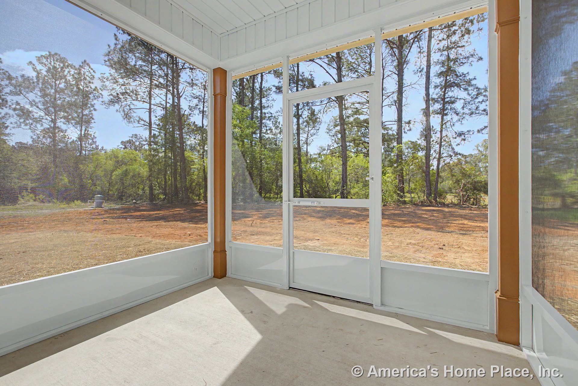 Screened-in porch with white trim and framing, central screen door, concrete floor, vertical support columns, ceiling panels, and outdoor wooded view.