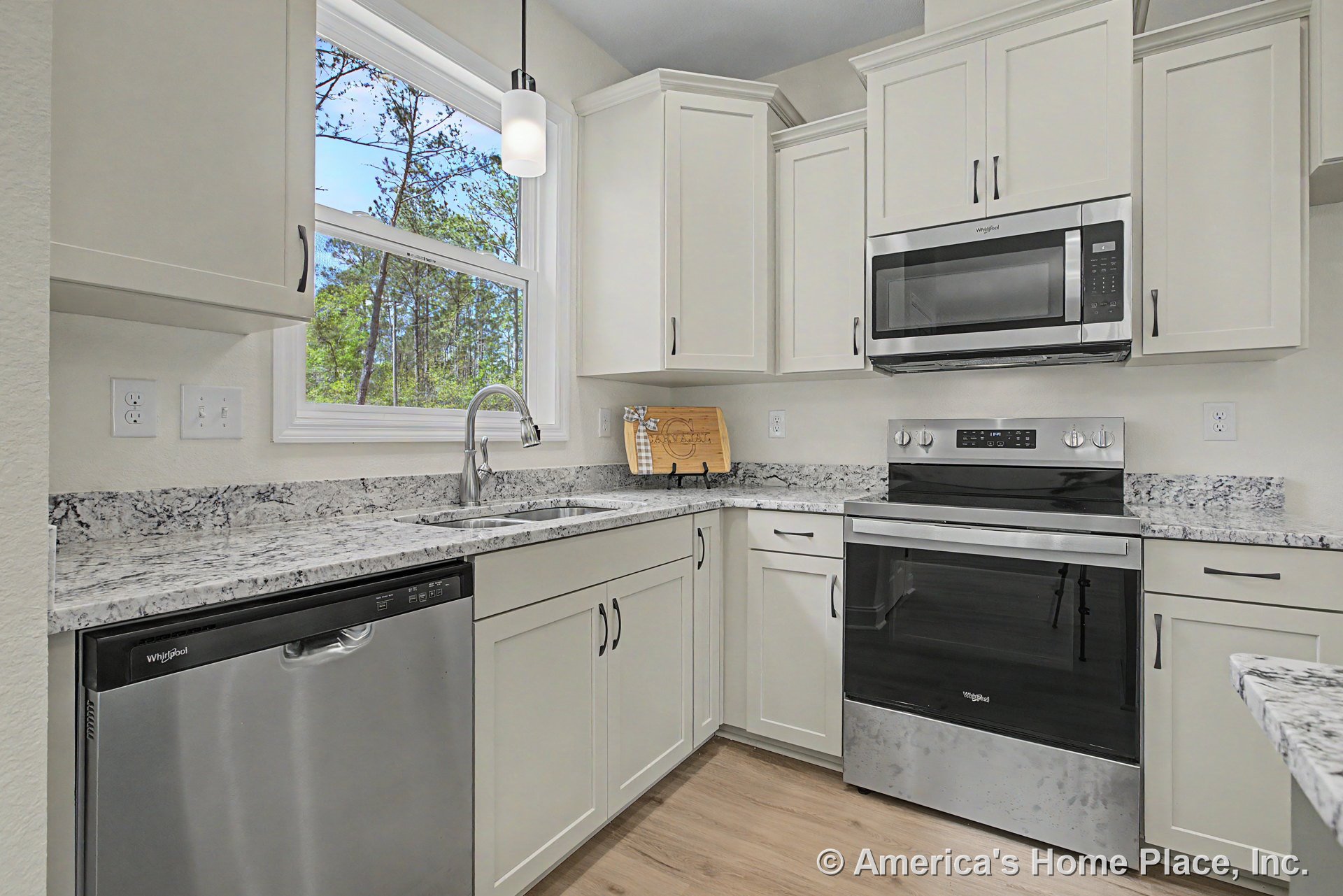White shaker cabinets with brushed nickel hardware, granite countertops and backsplash, double stainless steel sink beneath a large window, stainless steel dishwasher, oven, and