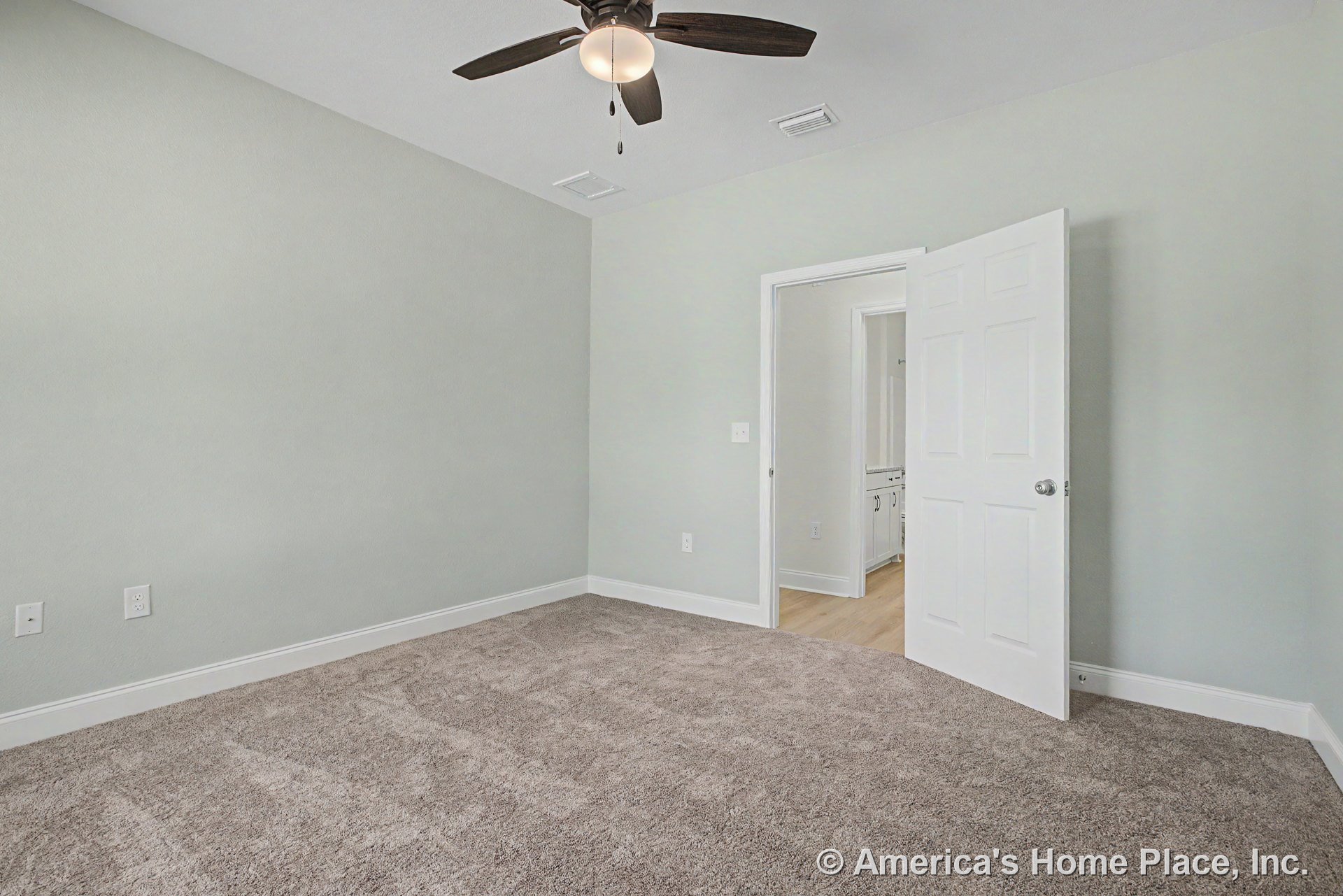 Bedroom with light gray carpet, white baseboards and trim, ceiling fan with integrated light, open paneled door leading to bathroom with visible cabinetry, neutral gray walls, and