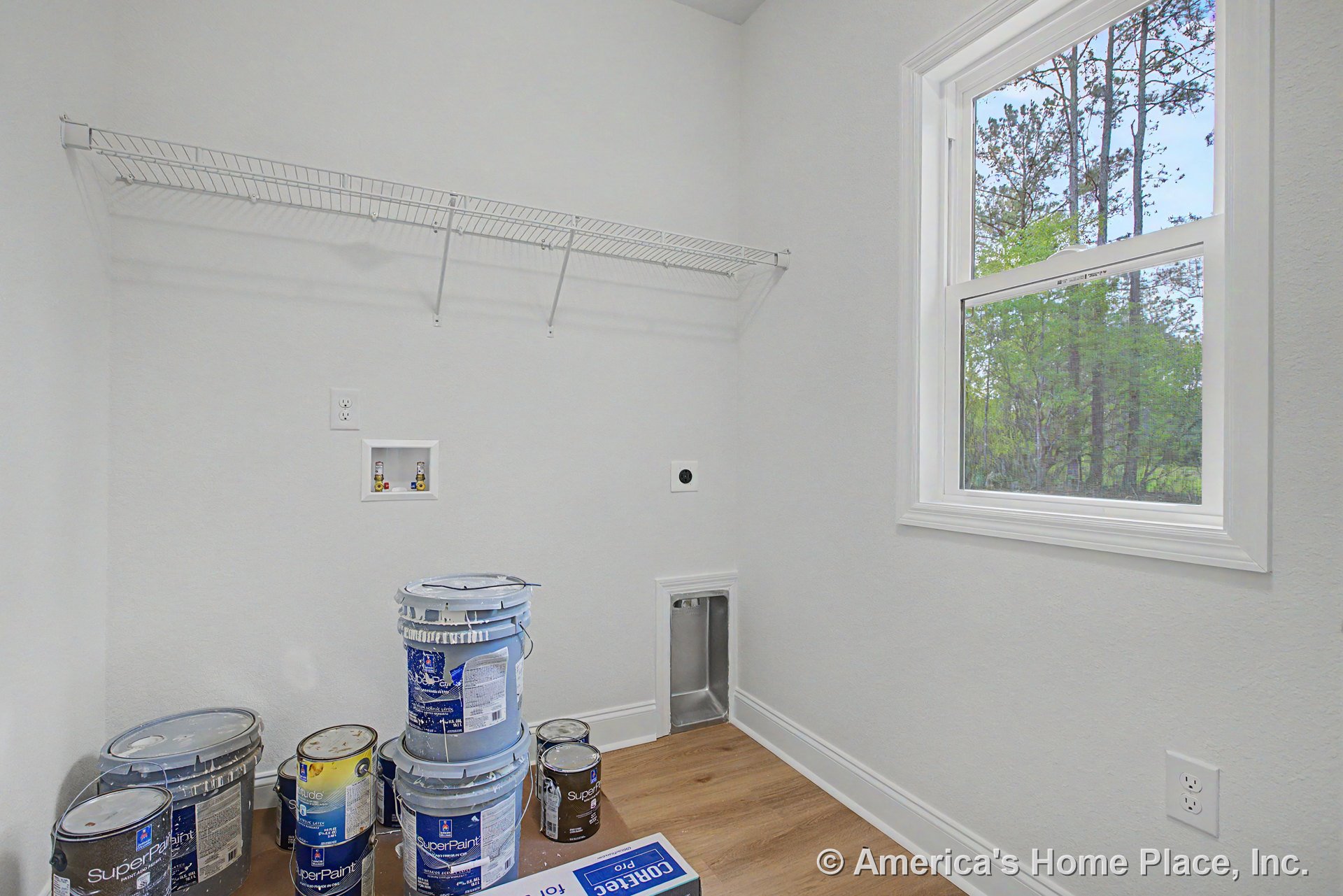 Laundry room with wire shelving, washer and dryer hookups, wood-look flooring, large window framed in white trim, baseboard, utility outlet, and laundry vent.