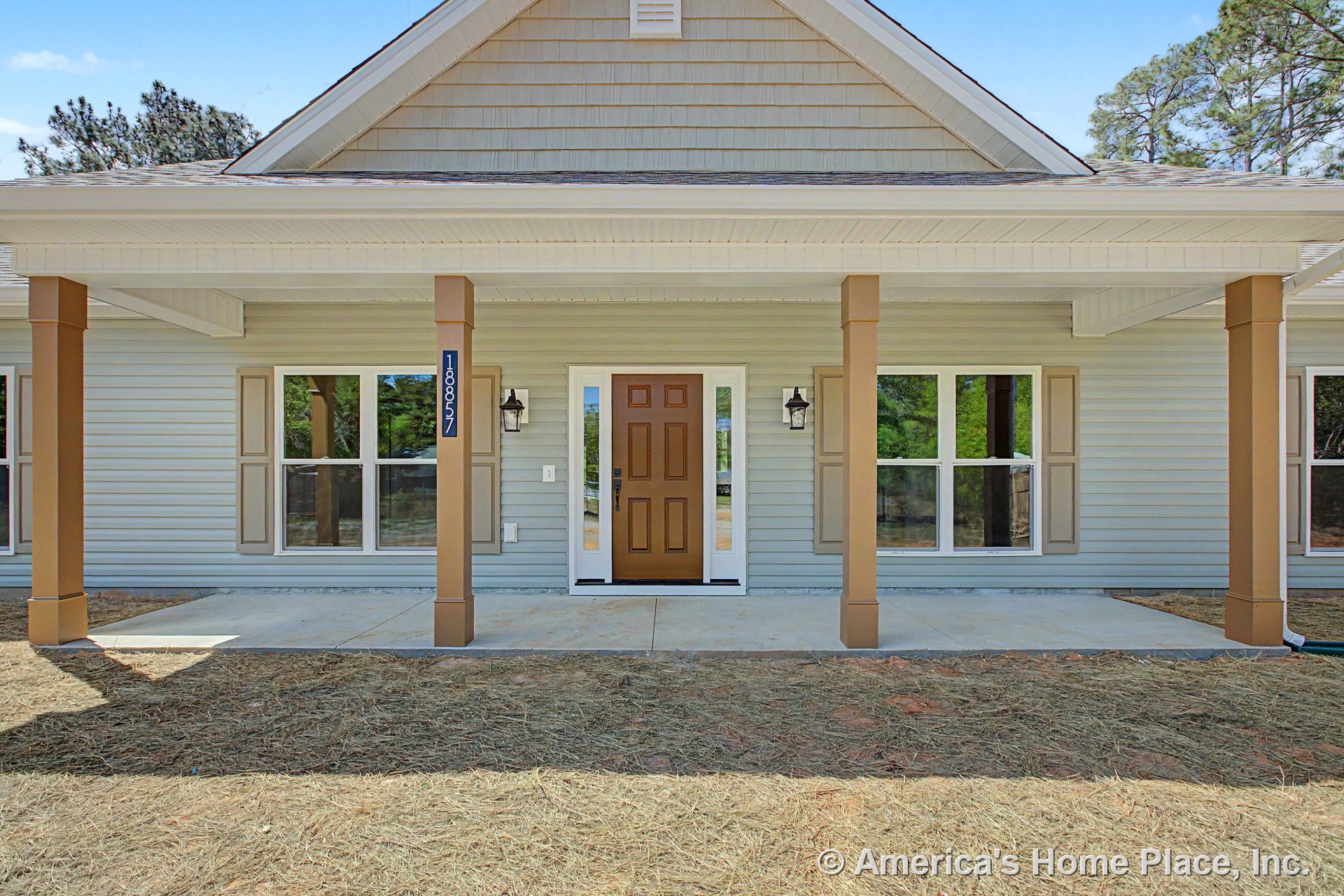 Covered front porch with four square columns, paneled entry door, double windows with shutters, horizontal siding, exterior wall lanterns, gable roof, concrete slab, and decorative