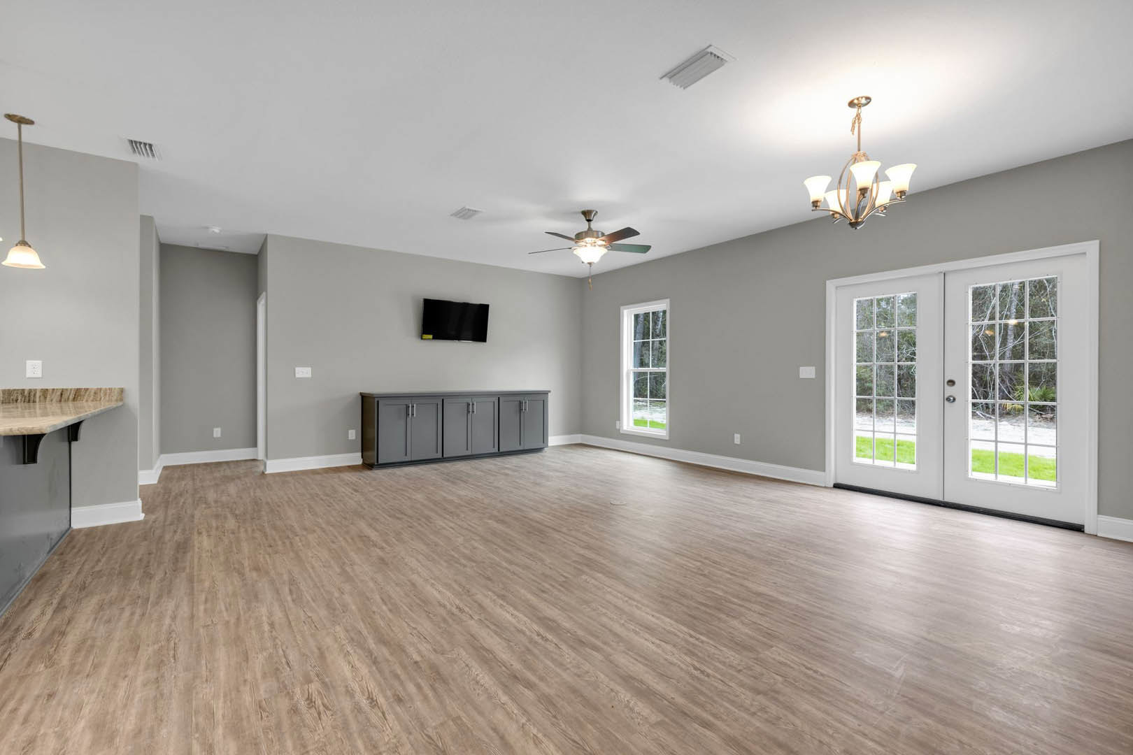 Wood flooring and white walls, ceiling fan overhead, grey cabinets with metal handles, double glass-paneled doors, window, yellow decor on white countertop