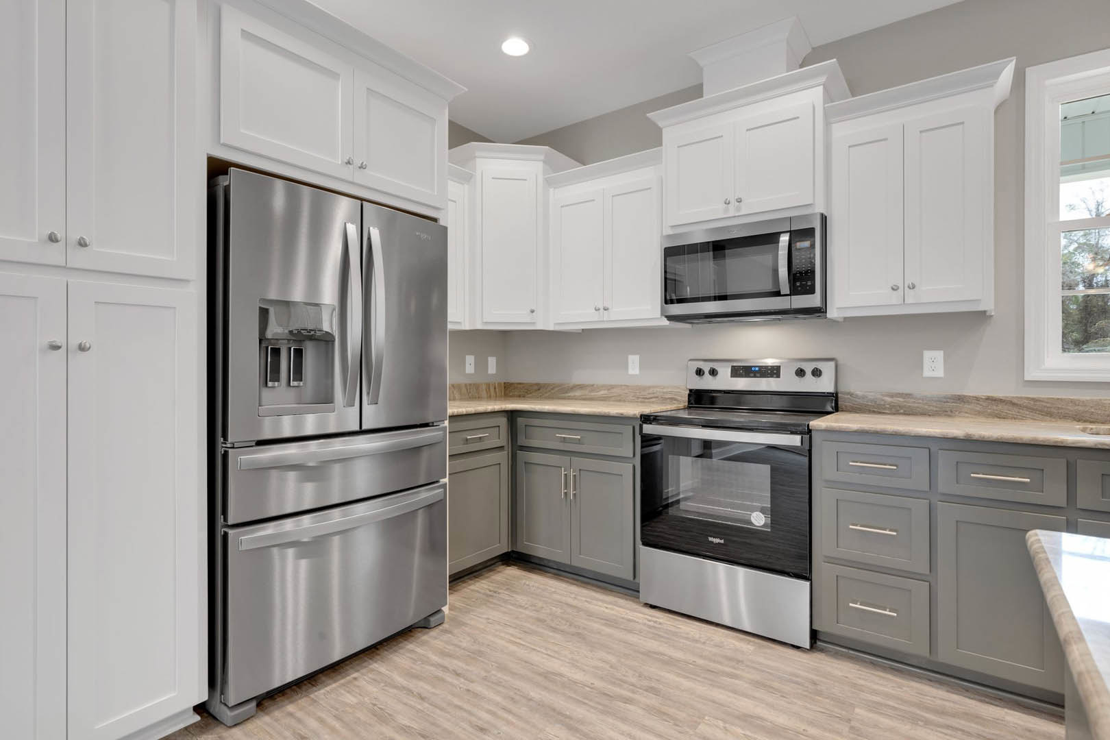 White kitchen cabinets, stainless steel refrigerator and oven, glass door microwave, stone countertop, window overlooking trees