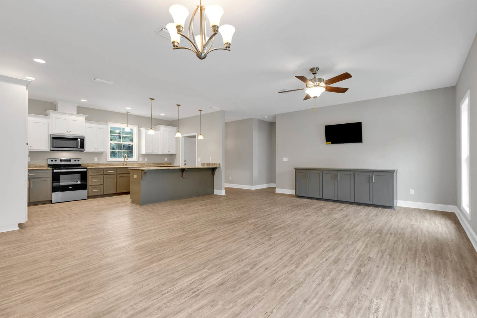 Spacious open-concept kitchen with central island, hardwood flooring, white cabinetry, stainless steel appliances including glass-door stove and built-in microwave, modern