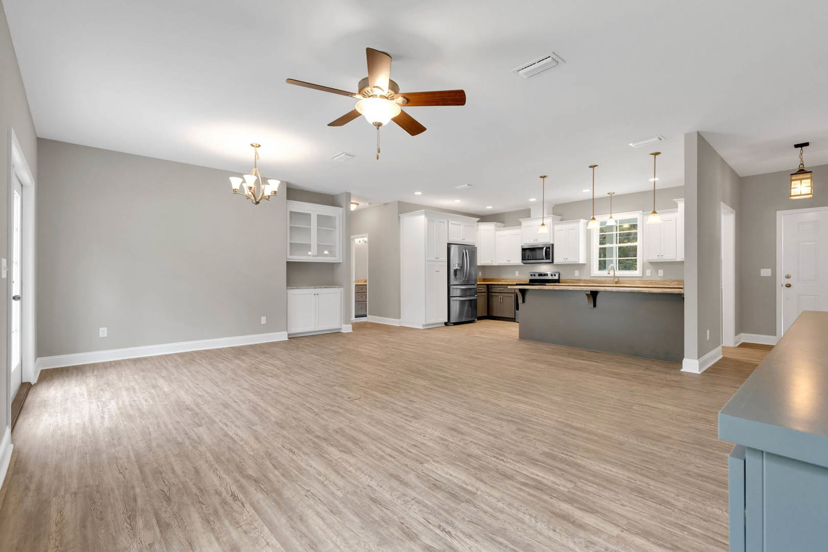 Spacious open floor plan featuring a kitchen with white cabinetry, stainless steel refrigerator, wood laminate flooring, dining area with a white table, ceiling fan with light, and