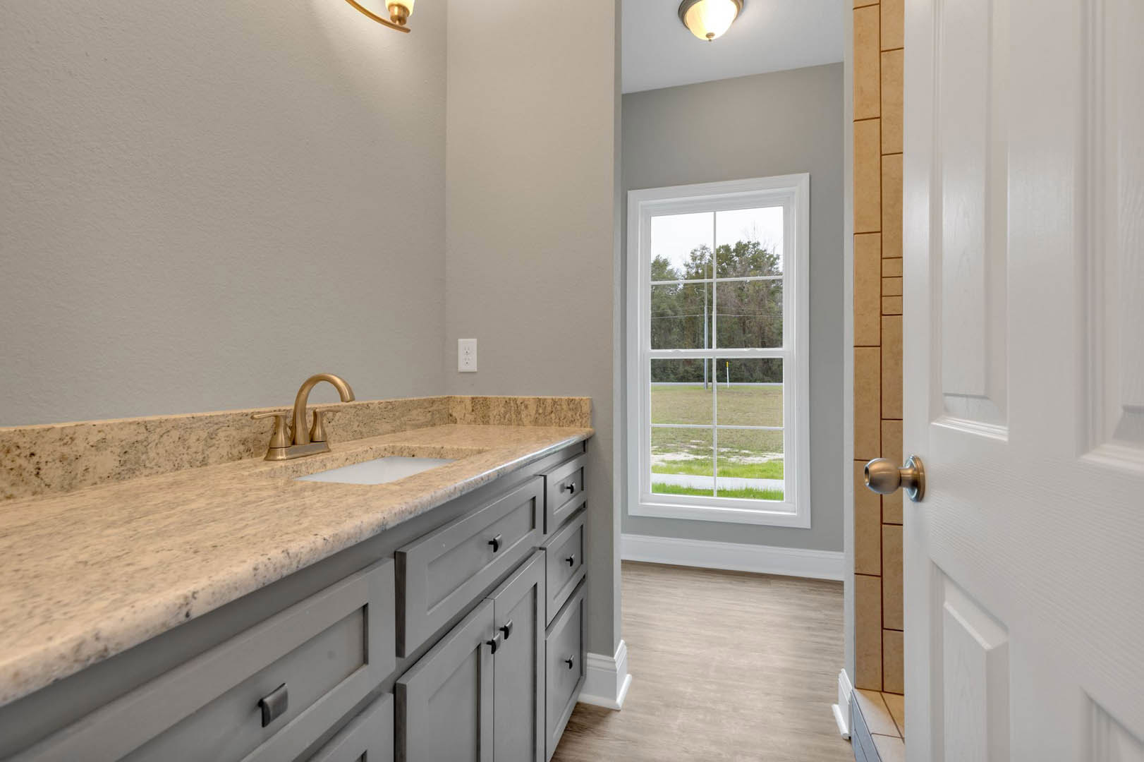 Bathroom with marble countertop, chrome faucet, wood floor with white trim, window overlooking a field, white cabinetry, and tile backsplash