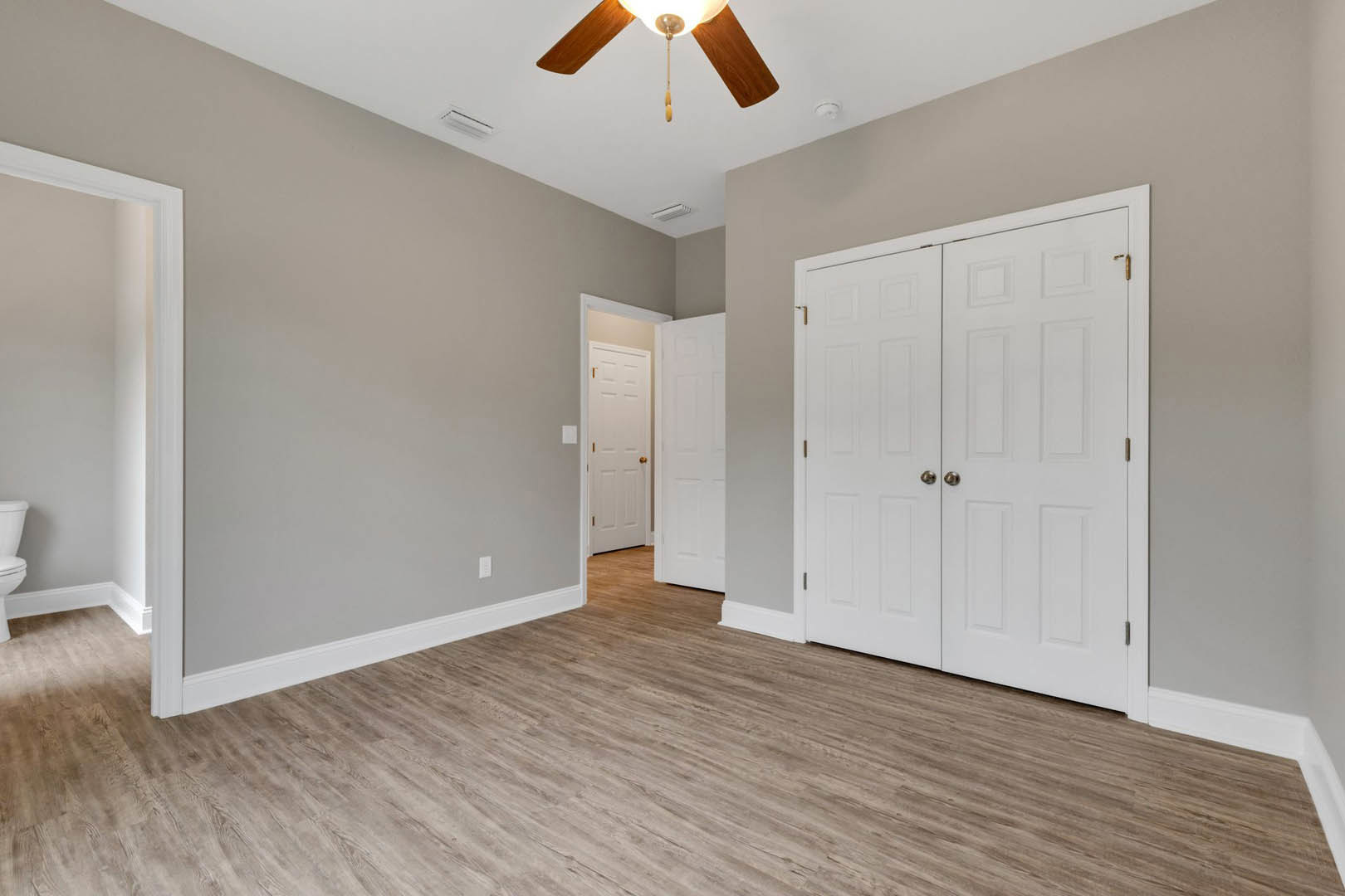 Room with wood flooring, white double doors featuring gold handles, white trim, and a ceiling fan with light fixture
