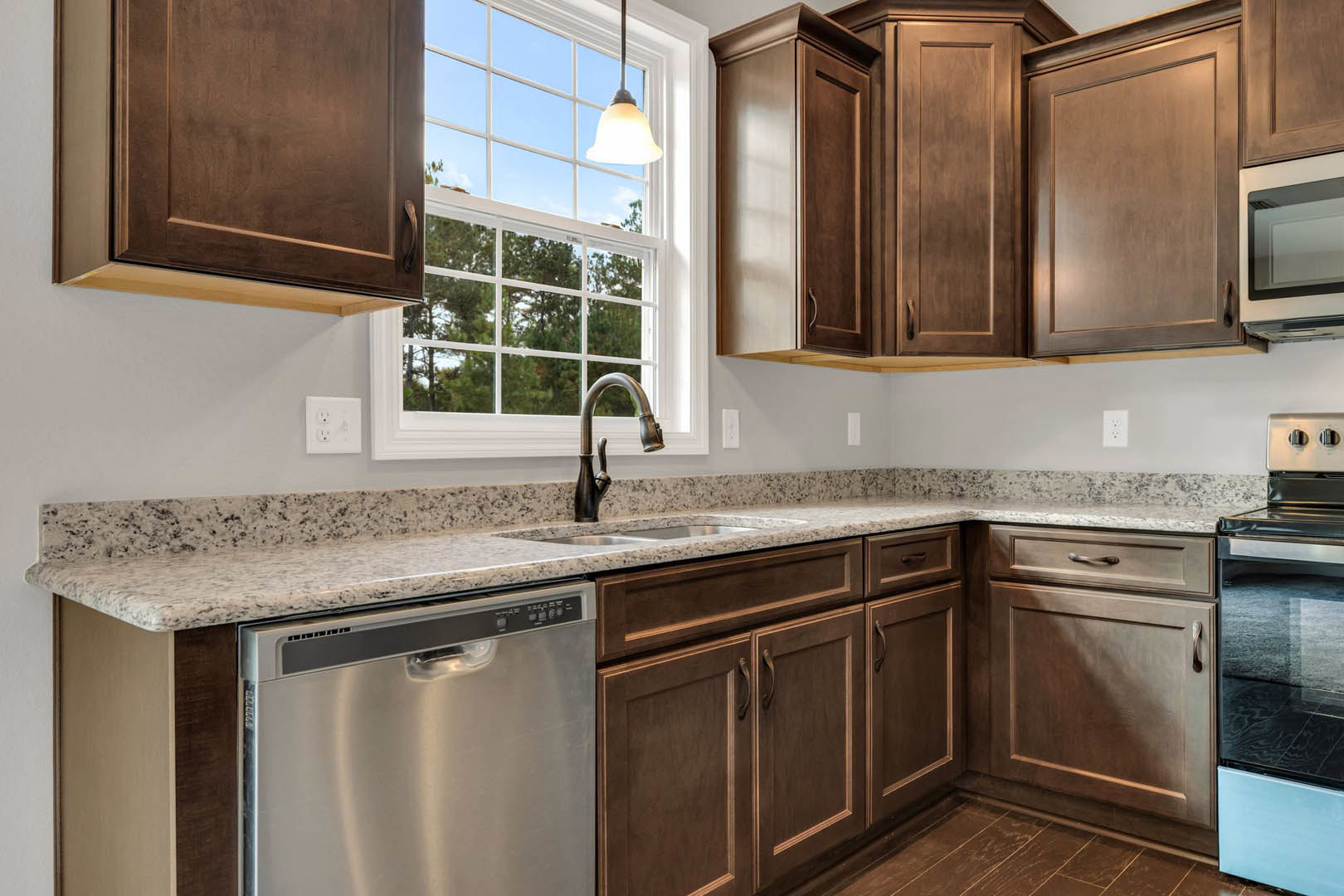 Marble countertop kitchen with stainless steel sink, built-in dishwasher, chrome faucet, white cabinetry, window with natural light, close-up of door and white wall outlet
