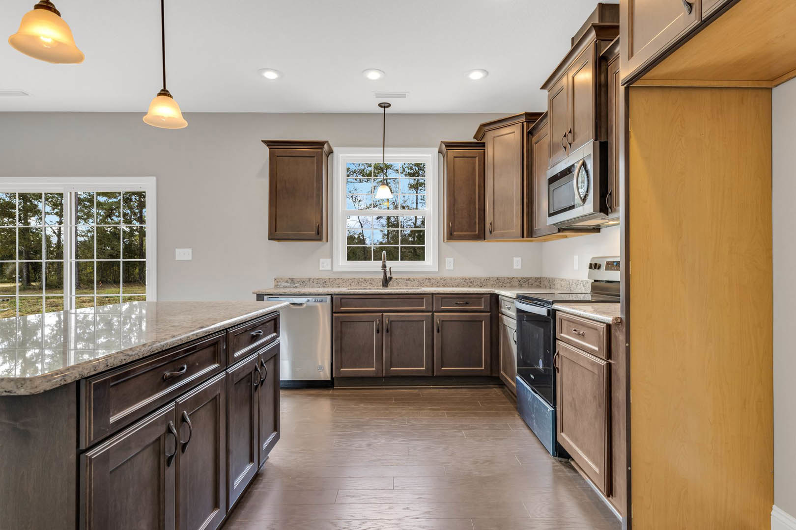 Dark wood kitchen cabinets, granite countertops, stainless steel sink, pendant light fixture, hardwood flooring, window with natural light, black-framed wooden door
