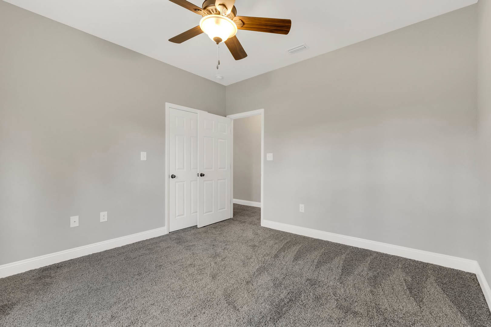 Carpeted room with white walls, ceiling fan with light fixture, white paneled door, crown molding, and baseboards