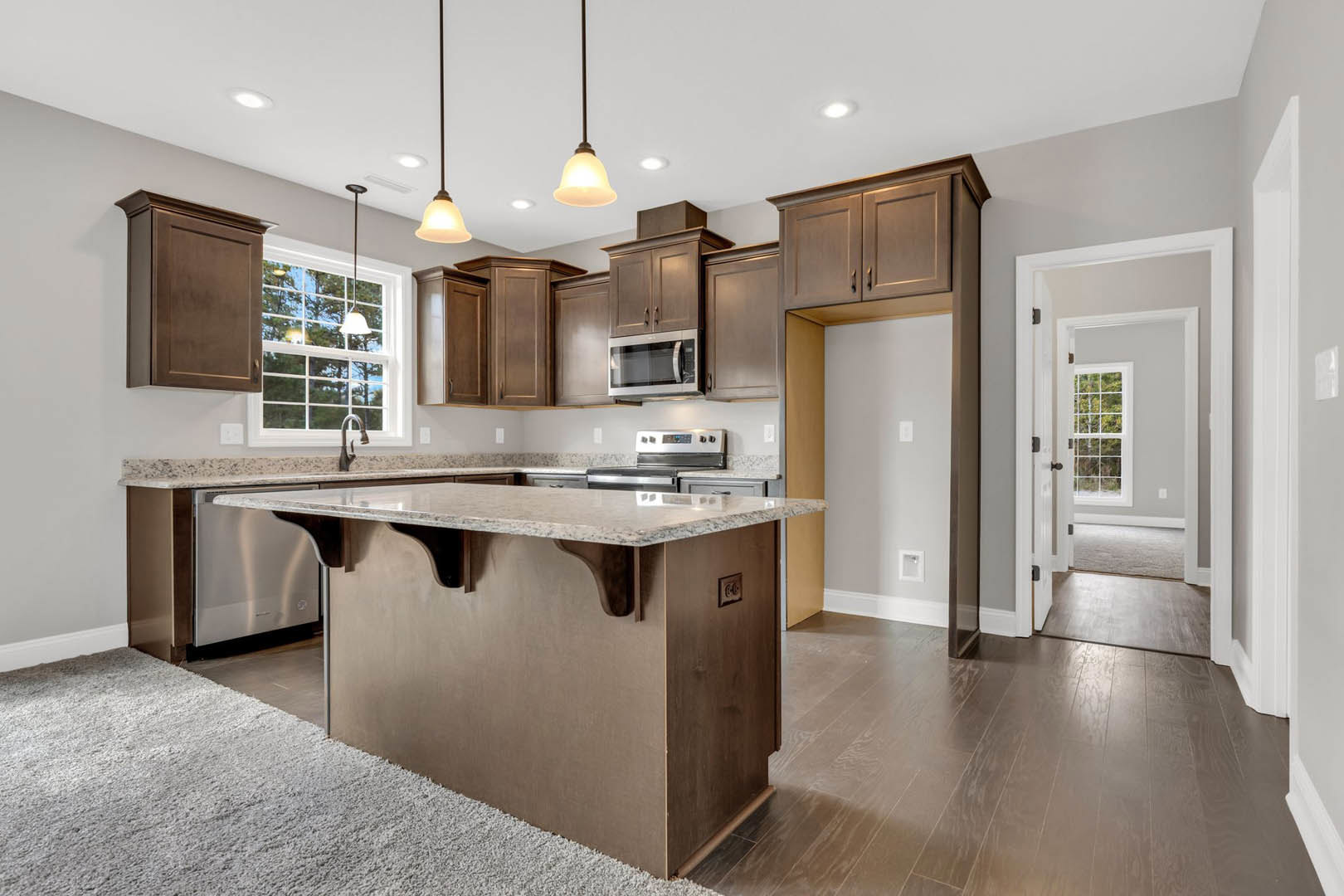 Spacious kitchen featuring a large central island with white countertop, built-in microwave oven with glass door, light wood cabinetry, stainless steel sink, and open doorway