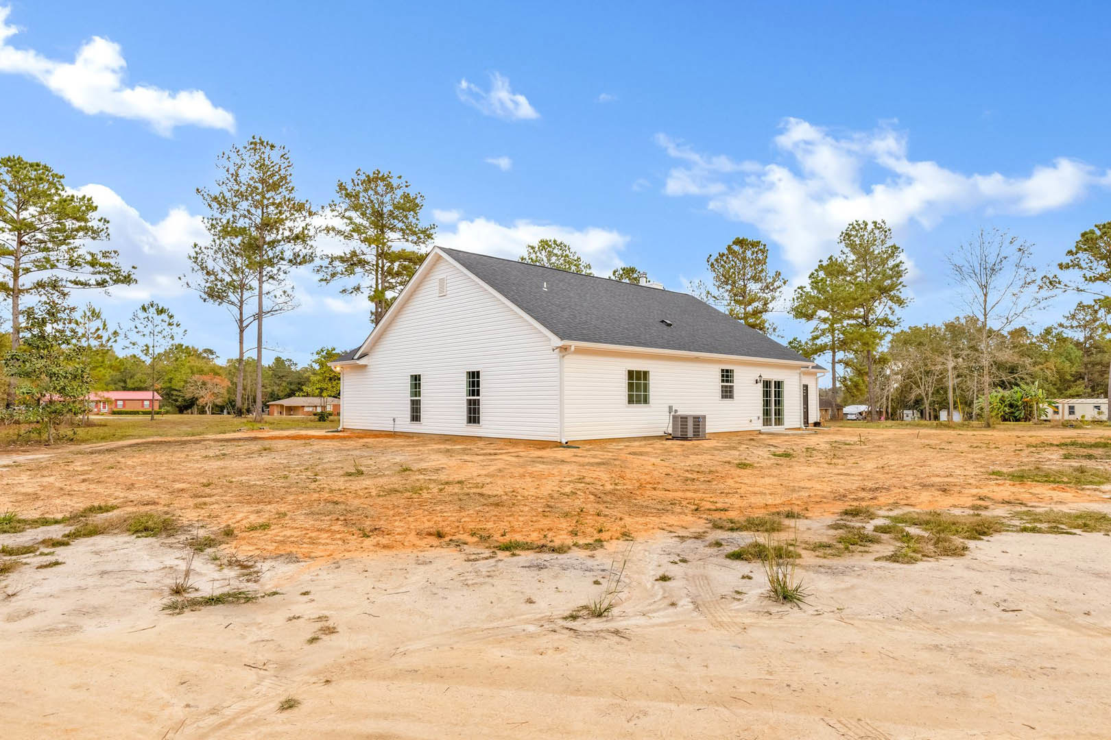 White house with black roof set on a dirt field, surrounded by green trees under a blue sky