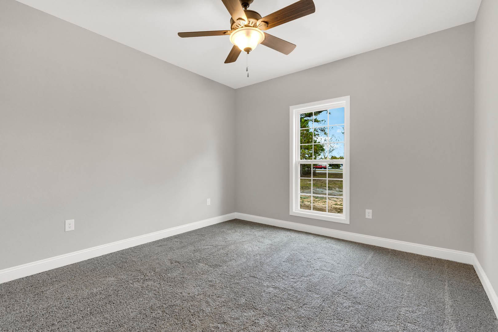 Ceiling fan with integrated light fixture mounted on white plaster ceiling above grey carpeted floor, window overlooking trees and red truck, white walls with crown molding