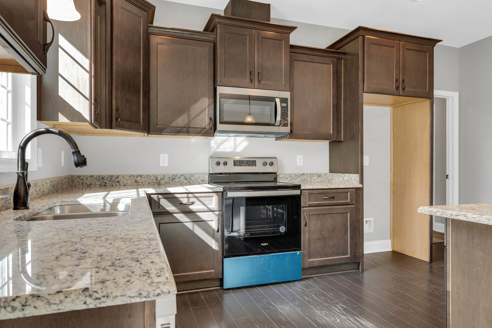 Dark wood kitchen cabinets, granite countertops, stainless steel oven, ceiling light fixture, chrome faucet, white door, undermount sink set in granite.