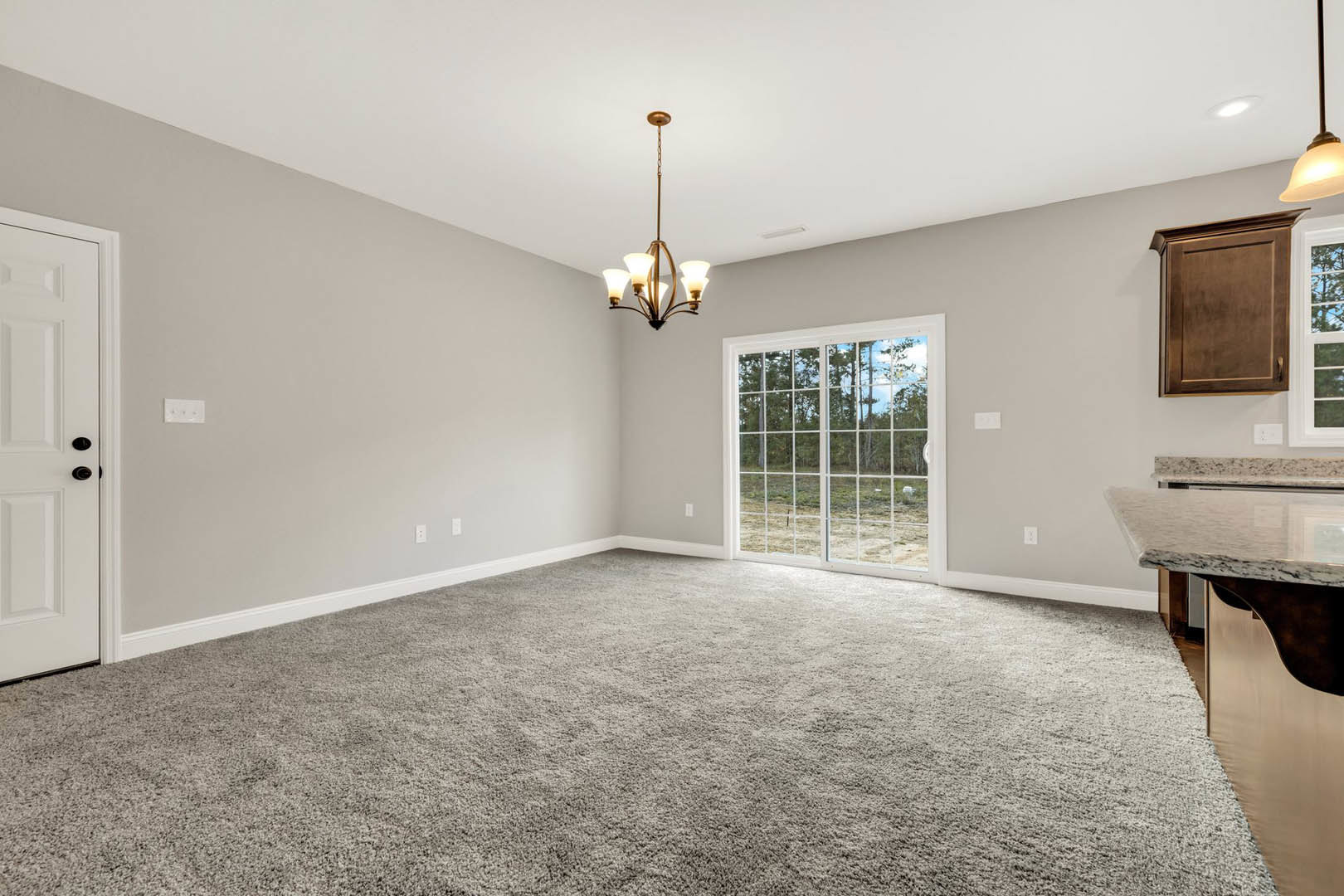 Modern living space featuring wood laminate flooring, white cabinetry, glass door opening to forest view, white interior door, contemporary chandelier, and neutral carpet.