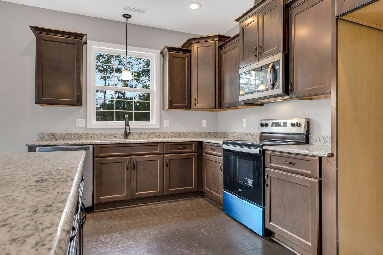 Kitchen featuring dark wood cabinetry, granite countertops, stainless steel microwave, under-cabinet lighting, and a window above the sink.