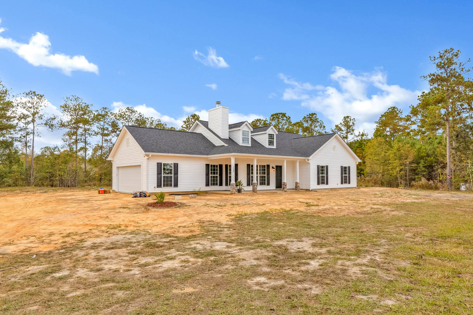 White siding house with black roof, front porch, black shuttered windows, white chimney, expansive grassy yard, and blue sky