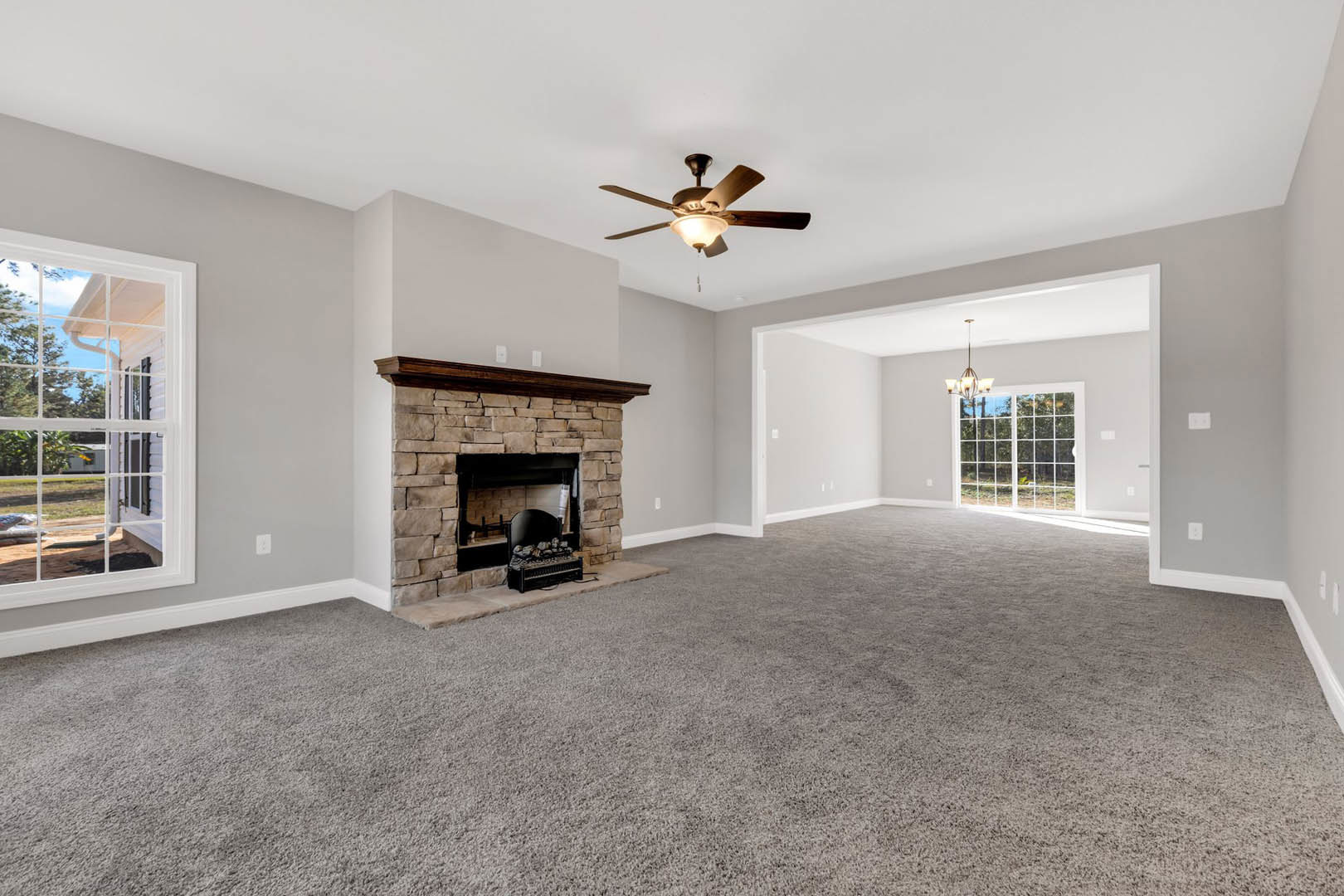 Carpeted living room featuring a black-framed fireplace with wood mantle, ceiling fan with light, and window overlooking neighboring house